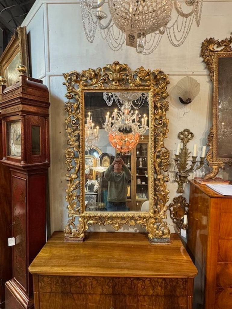 Questo specchio in legno intagliato e dorato del XIX secolo, proveniente da Firenze, Italia, presenta un design lussuoso che mette in mostra intricati dettagli in legno intagliato e dorato. La cornice a specchio emana eleganza e raffinatezza,