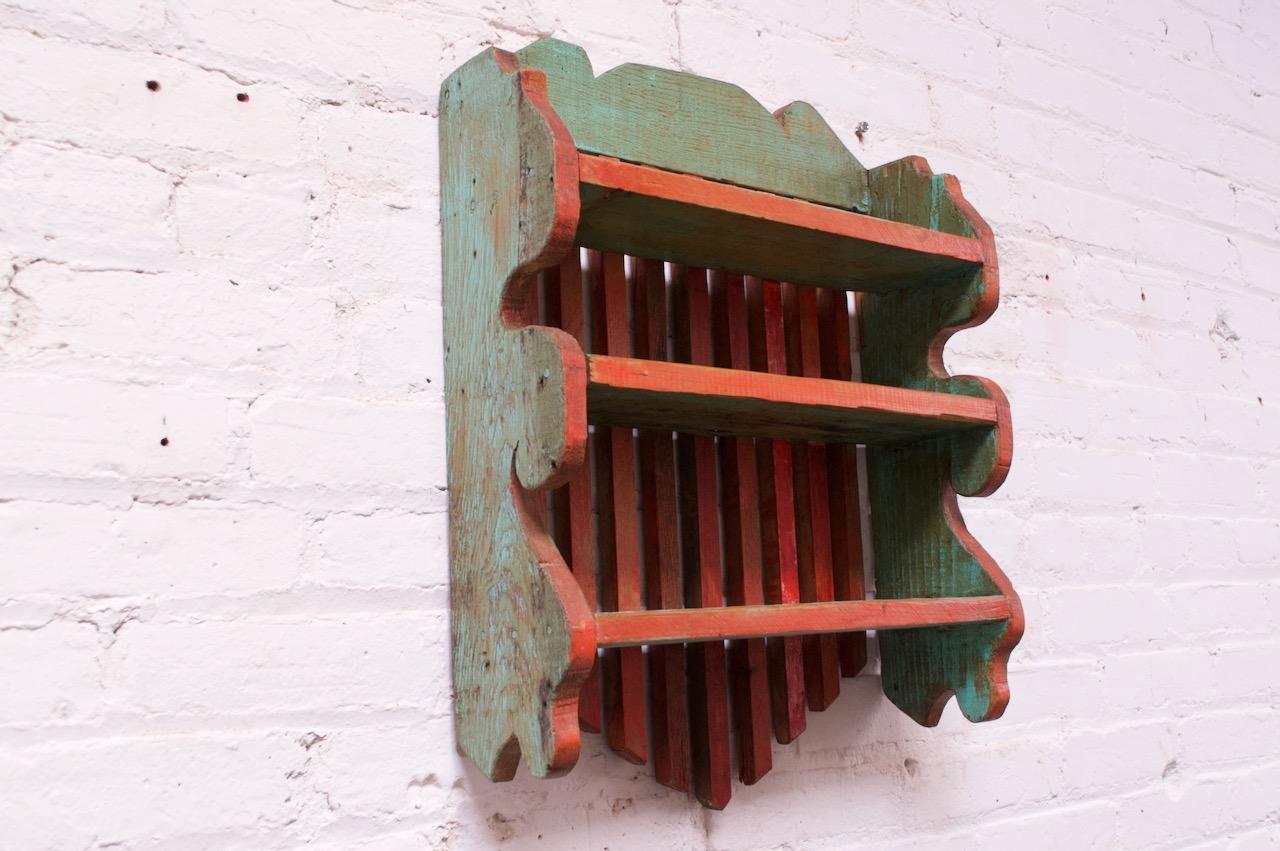 Hand painted and carved small oak shelf (circa 19th century, USA) composed of a simple slatted back with carved border in brick red and mint green. Three, shallow surfaces accommodate smaller objects.
Lovely, natural patina with wear consistent