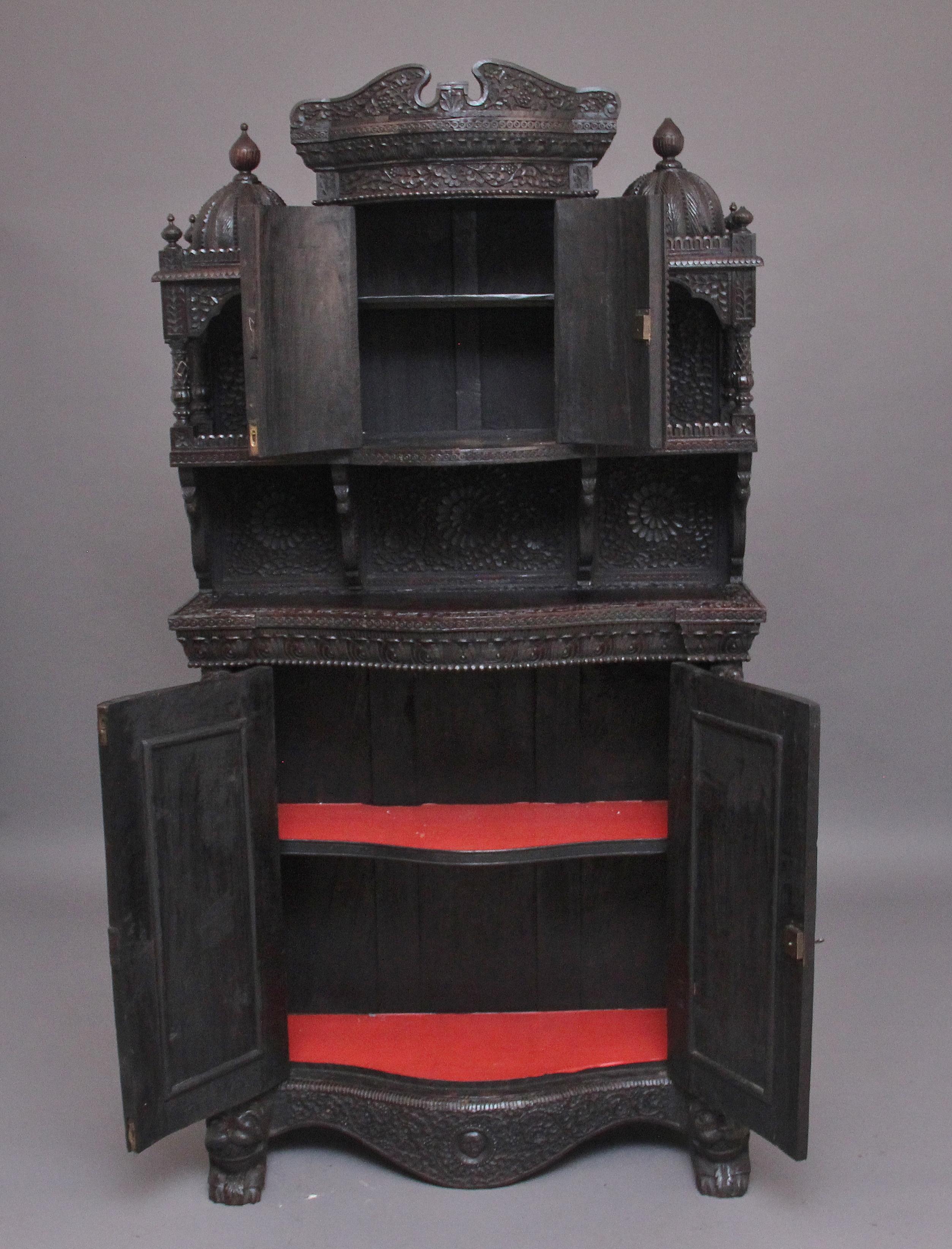 A superb quality mid 19th century carved Anglo - Indian cabinet influenced by Brighton pavilion, the shaped arched pediment above a two door cupboard opening to reveal a single fixed shelf inside, a shelf either side with decorative loose bold