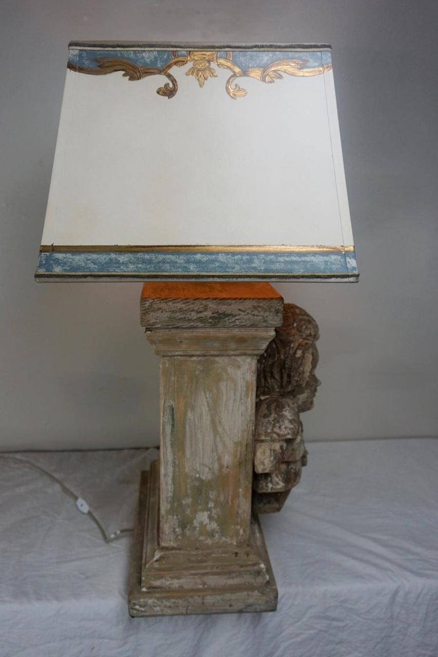 Lámpara personalizada de madera tallada a mano con cara de querubín recién cableada con vela de cera goteante. La lámpara está coronada por una pantalla rectangular de pergamino pintada a mano. Acabado pintado desgastado con bonitos desgastes.