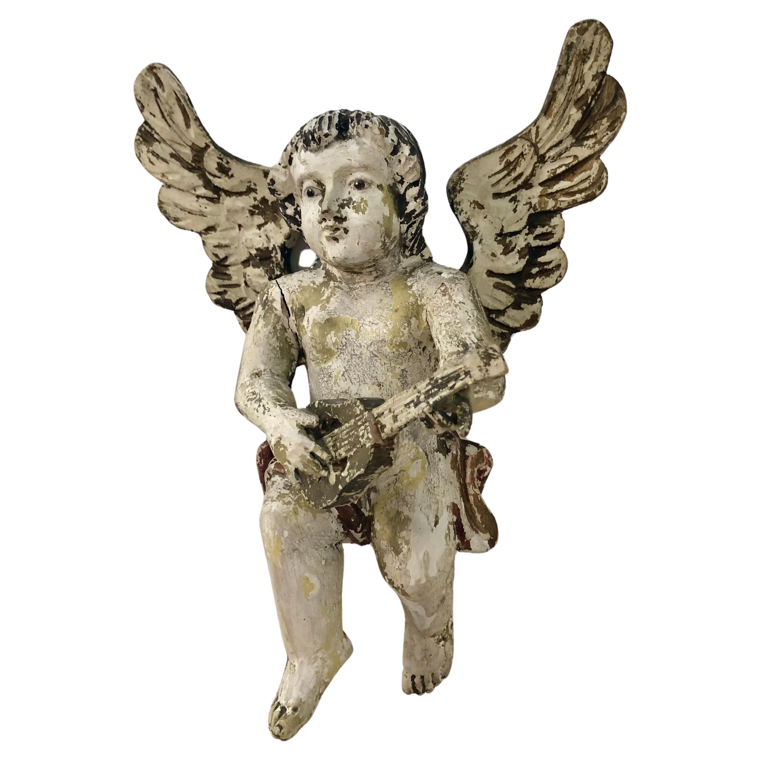 A beautiful early 19th Century polychrome winged cherubim, or angel, holding a guitar or mandolin. This angel would have most probably hung in a church.
The angel is carved and gessoed with white overpaint, gilding, and glass inset eyes.
Most