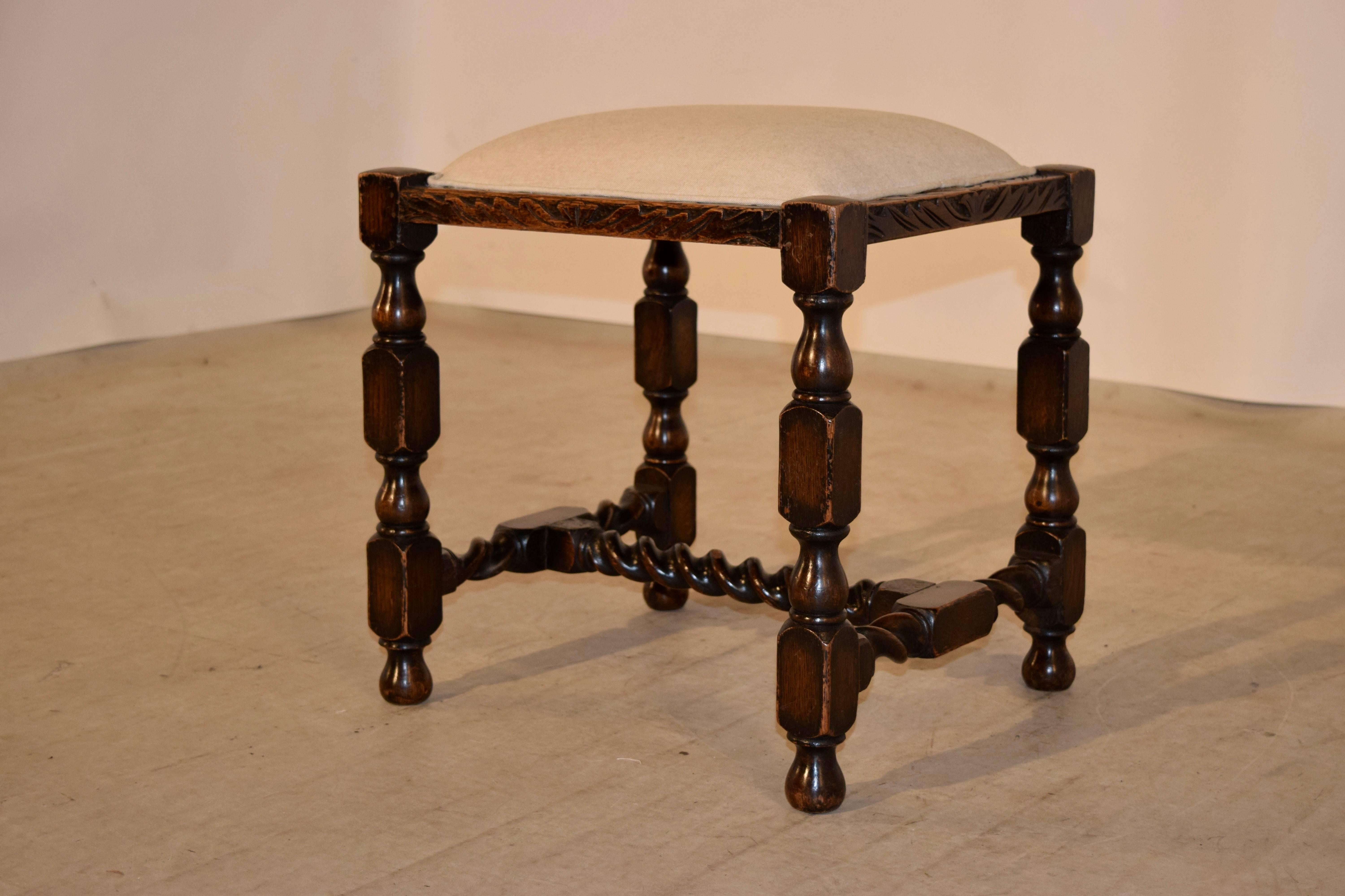 19th century English oak stool with a hand-carved decorated border around the seat, following down to hand turned legs and barley twist stretcher, resting on hand turned feet. The seat has been newly upholstered in linen and finished with single