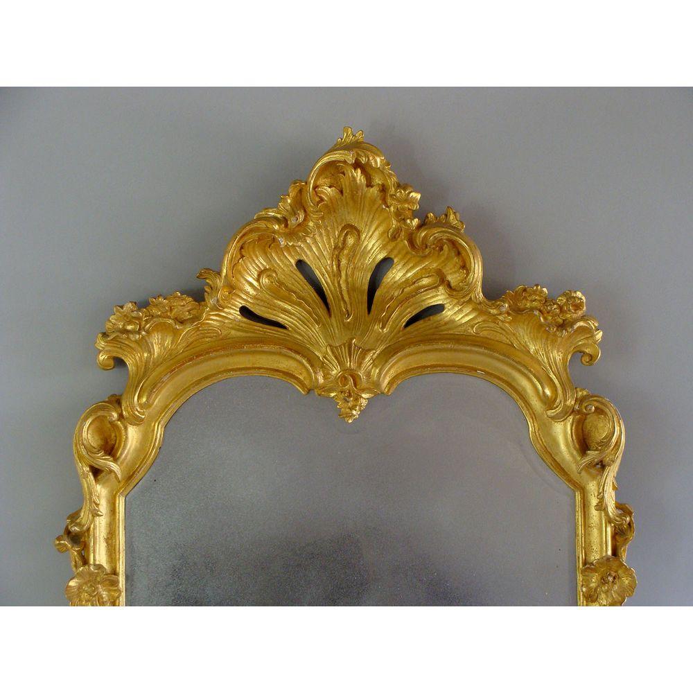 An impressive carved giltwood and gesso pier glass mirror.
19th century.
With a bold shell cresting and trailing flowers in the margins.
Divided, beveled plate.

This chic antique pier glass, or looking glass, has been historically re-gilded to