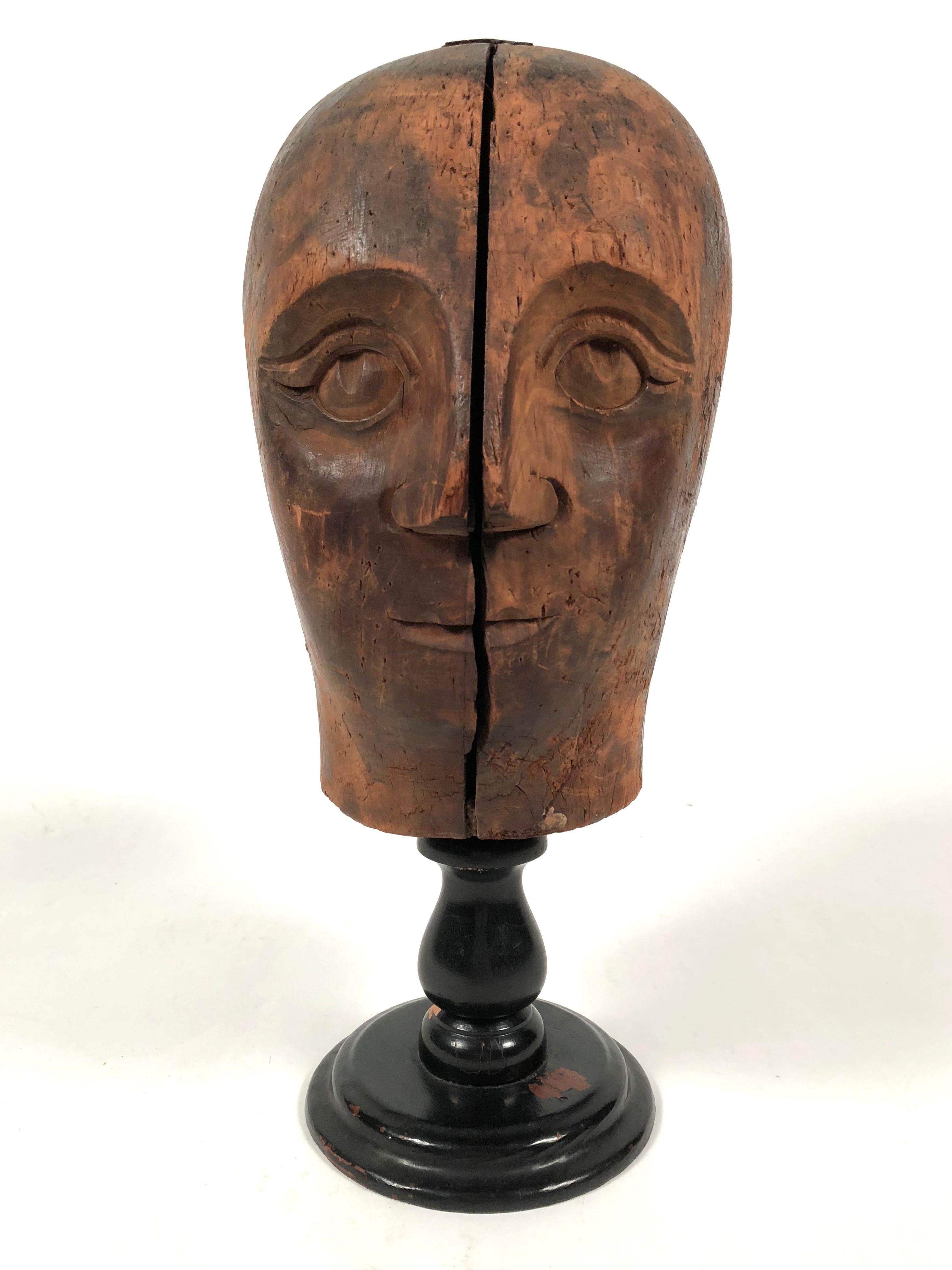 A 19th century Folk Art carved wooden head of a man, likely a hat display form 19th century, carved from two joined wooden segments, with well delineated facial features. Mounted on a black painted turned wooden stand.

 