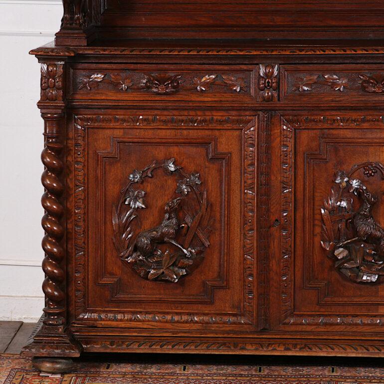 Heavily carved French Henri II buffet or hunt cabinet  ‘deux corps’ in oak, the lower doors with detailed carved leaves and hunting dogs, the upper cabinet with glass doors and raised on a pair of fierce gargoyle supports. Barley twist columns to