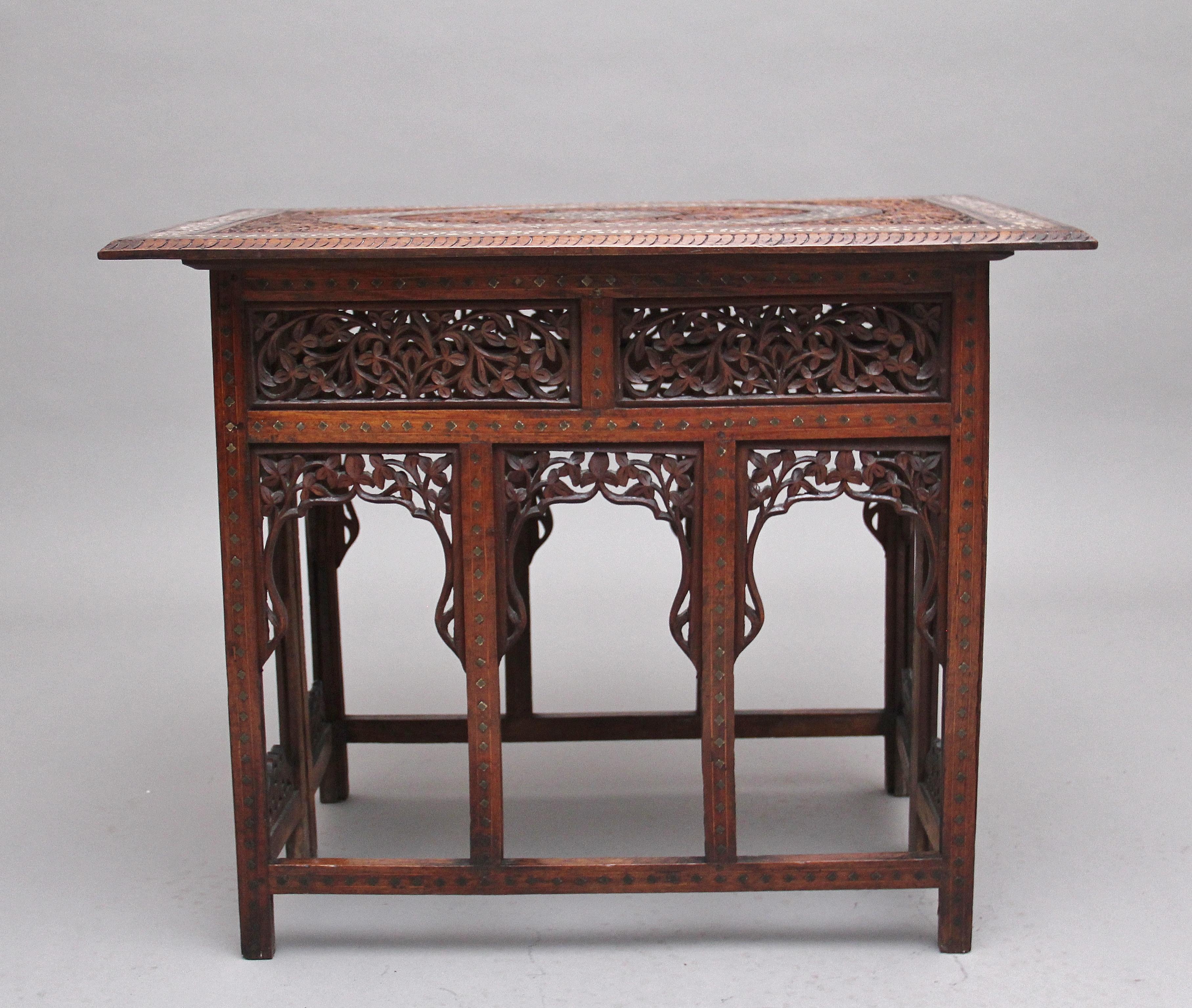 19th century Indian folding teak occasional table, the highly decorative and profusely carved top incorporating various vines and foliage, central oval border with bone inlay, carved moulded edge, the square base united with stretchers, the frieze