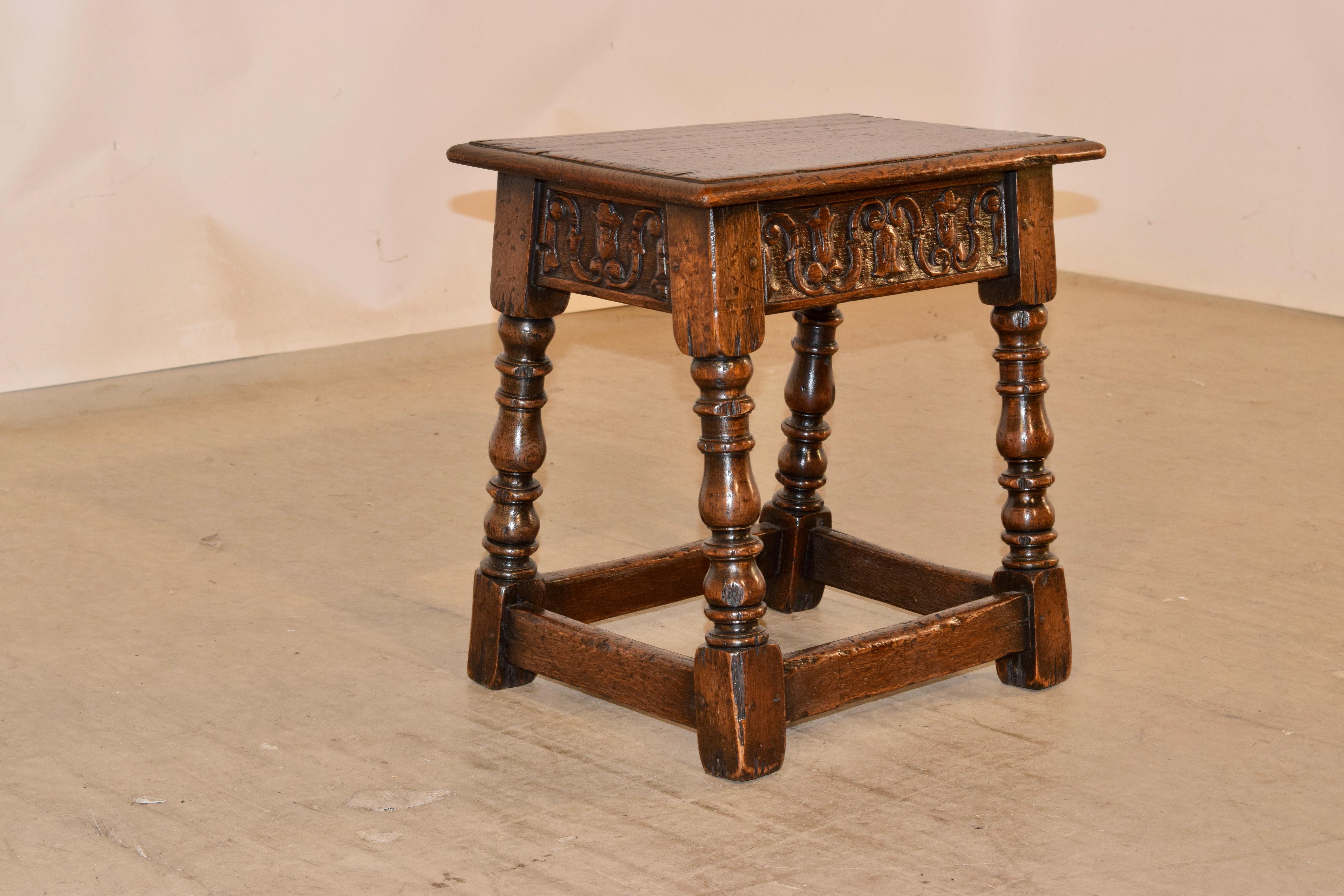 19th century oak joint stool from England with a beveled edge around the top, following down to a hand carved decorated apron with lovely floral and scrolls and supported on hand turned and splayed legs, joined by simple stretchers.
