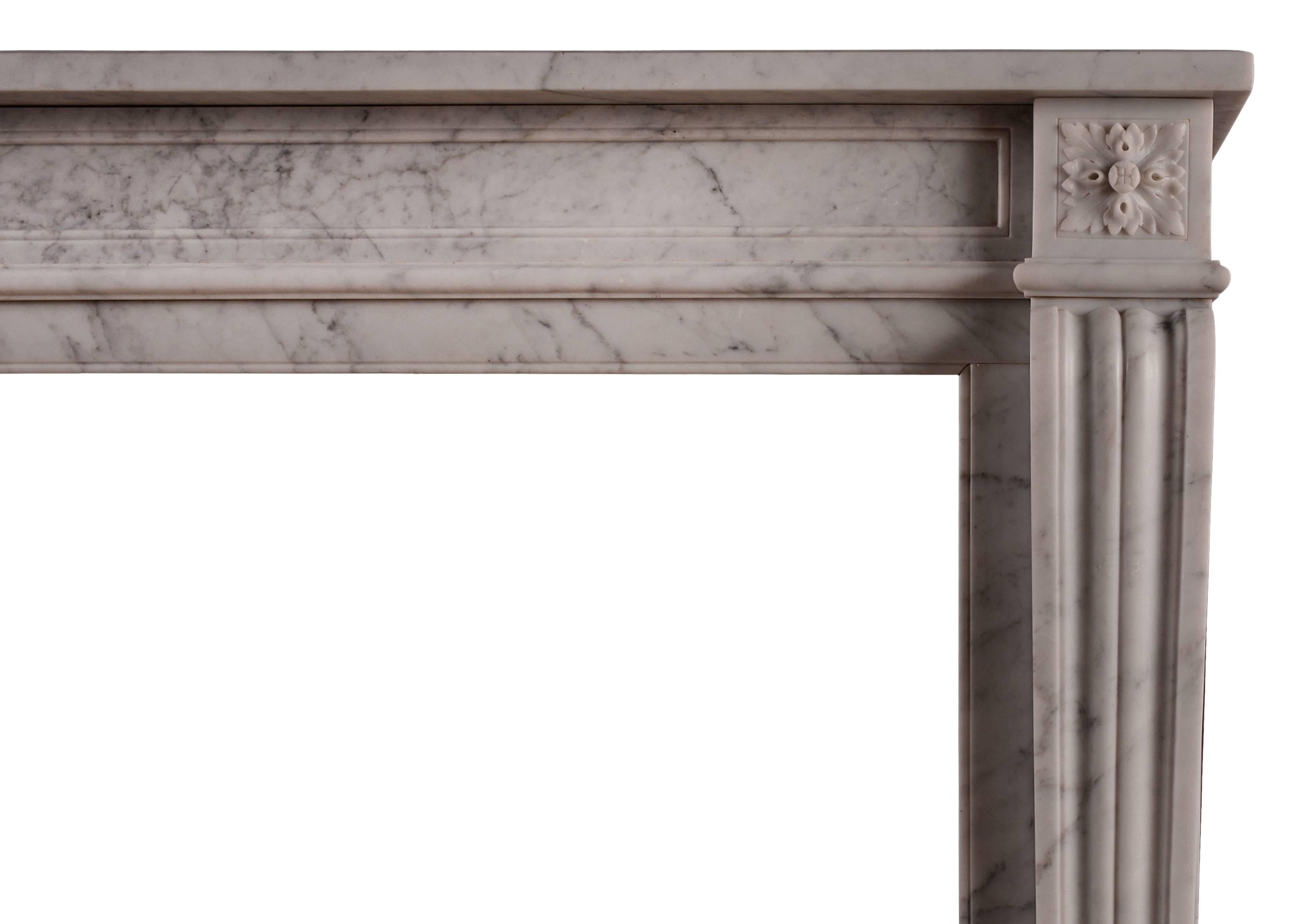 A Carrara marble fireplace in the Louis XVI manner. The shaped jambs with flutes throughout, surmounted by square carved paterae. Panelled frieze, surmounted by plain shelf. A restrained and elegant piece with good proportions for a study or smaller