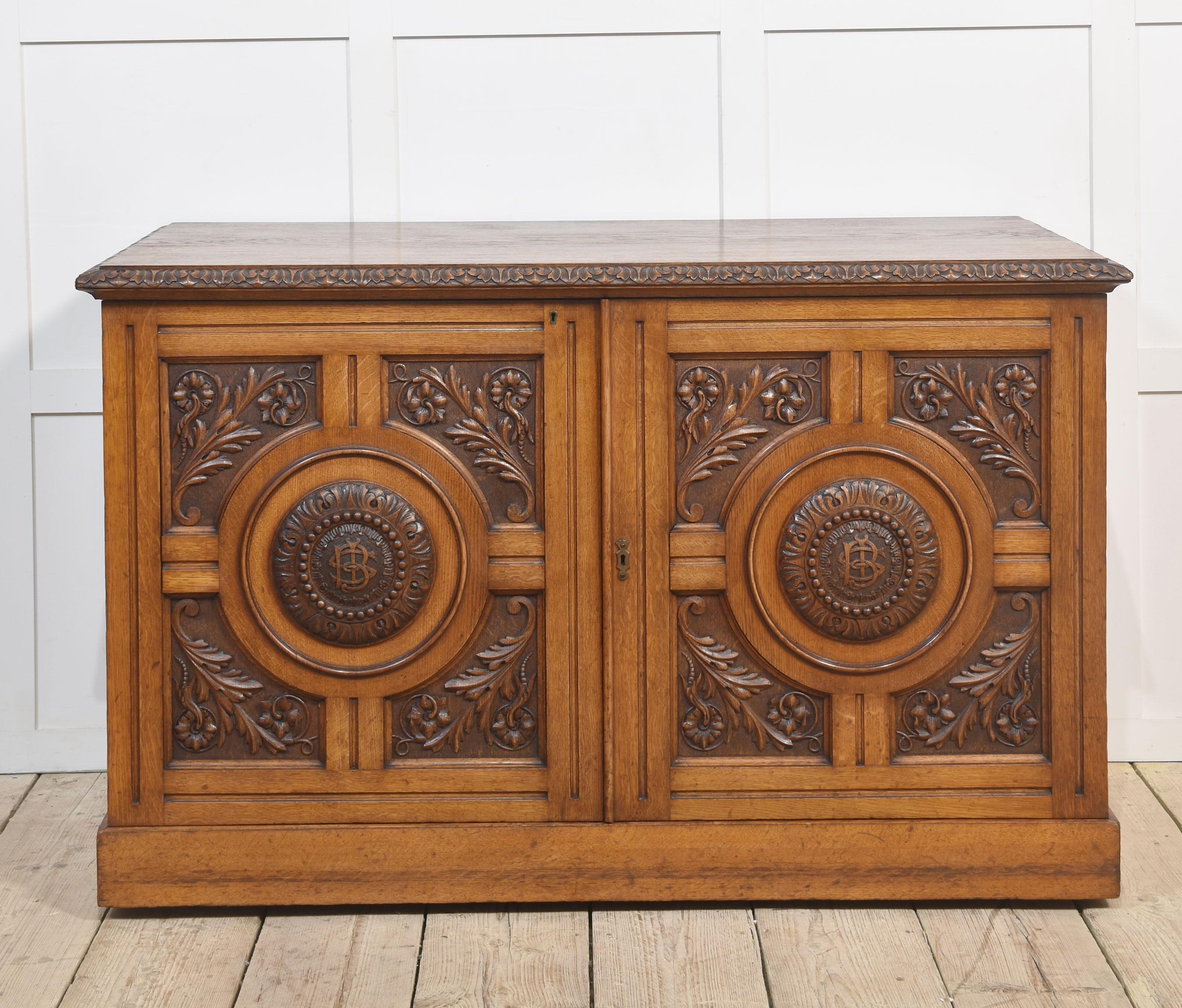 19th-century cabinet, the large rectangular well-figured oak top having a molded edge. Above two finely carved doors with foliated scrolling detail. The door opening to reveal two banks of five graduated drawers with recessed brass handles. All