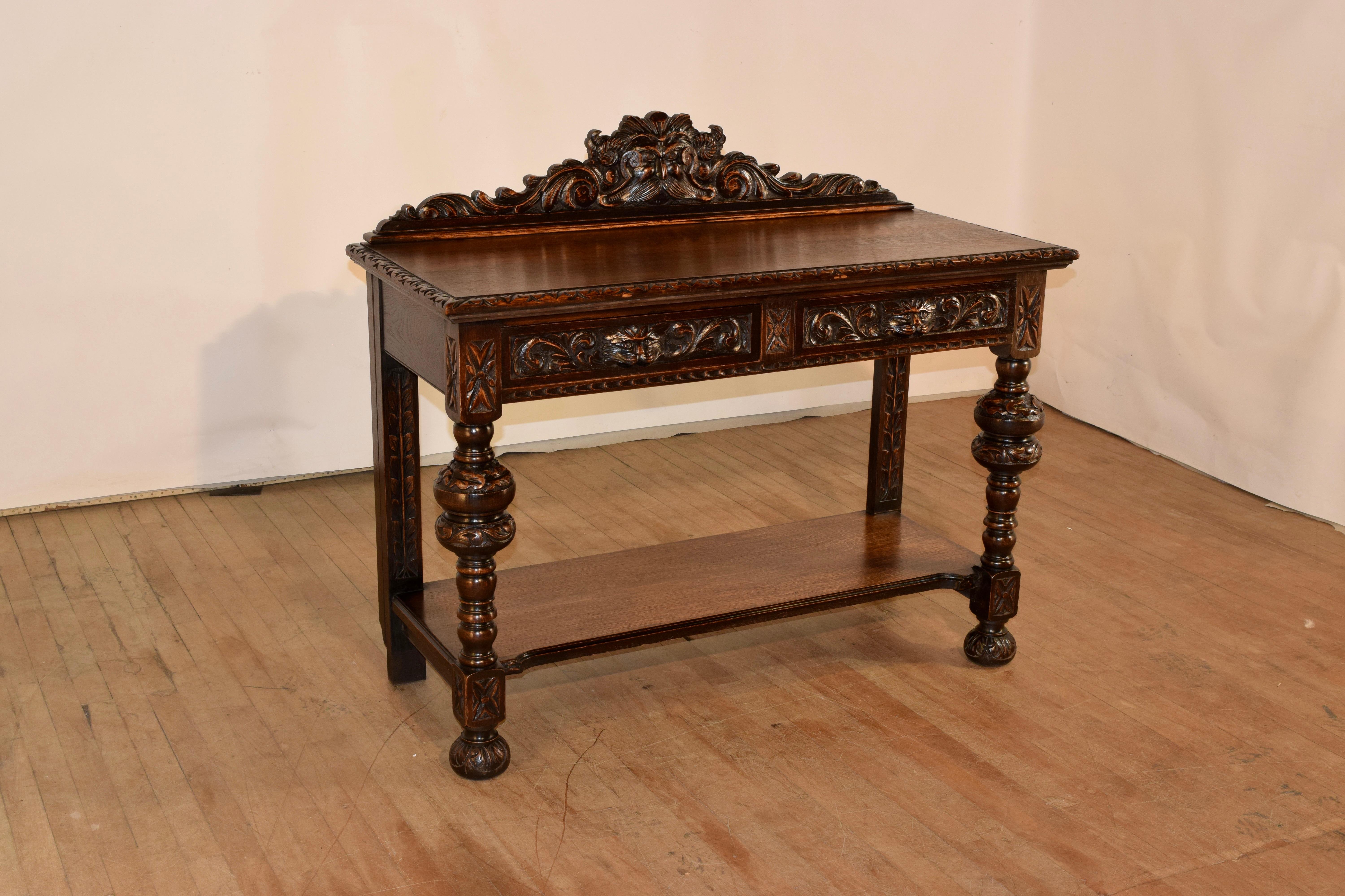 19th century oak console table from England with a wonderfully detailed hand carved backsplash over the top of the table, which has a beveled and carved decorated edge and simple sides. The front of the piece has a carved apron with two drawers,