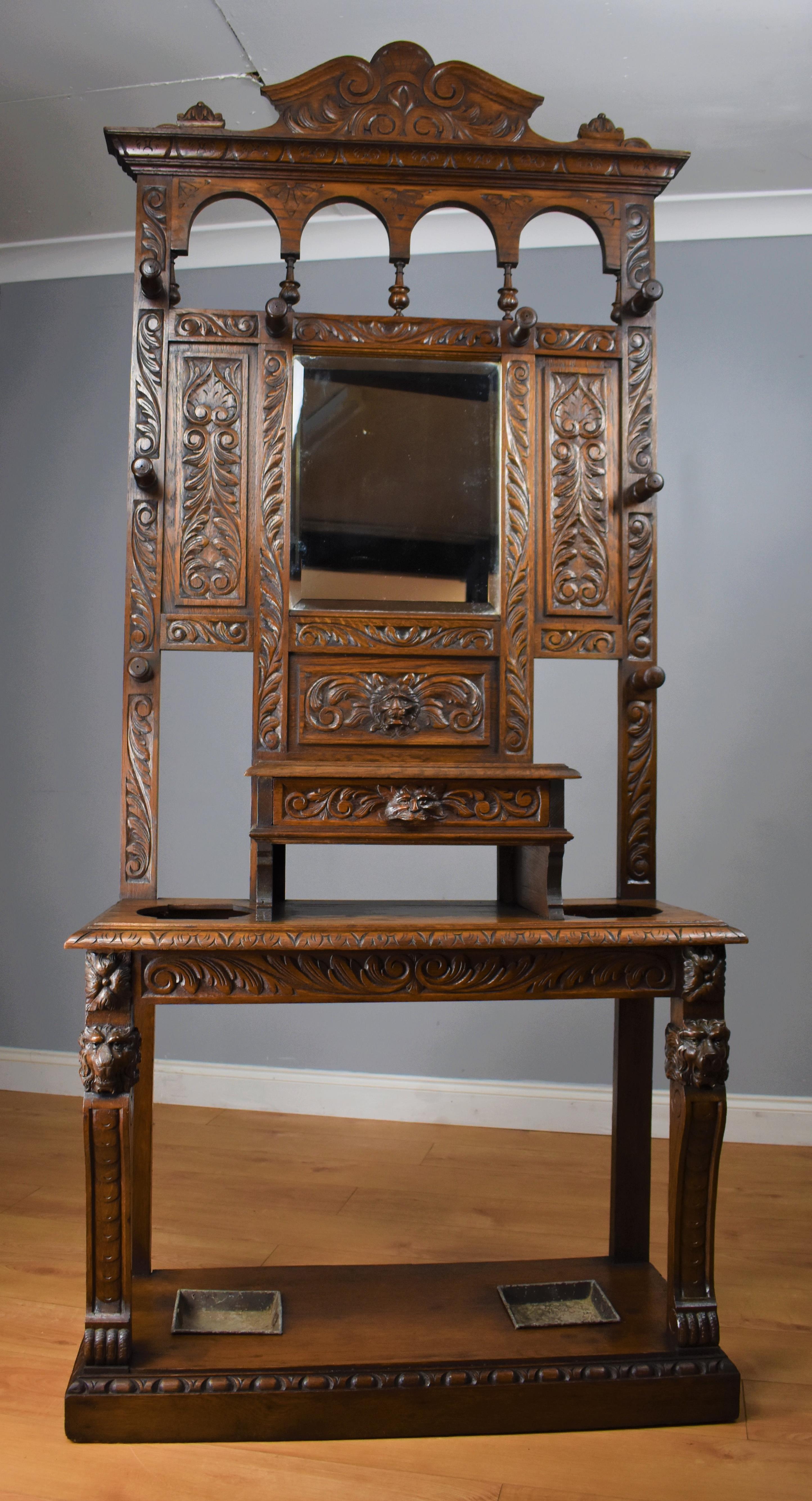 Late 19th century oak carved Flemish style hall stand in good condition having been polished by hand. The hall stand has a carved pediment (pediment is removable) to the top with a bevelled mirror to the centre with turned coat hooks either side,