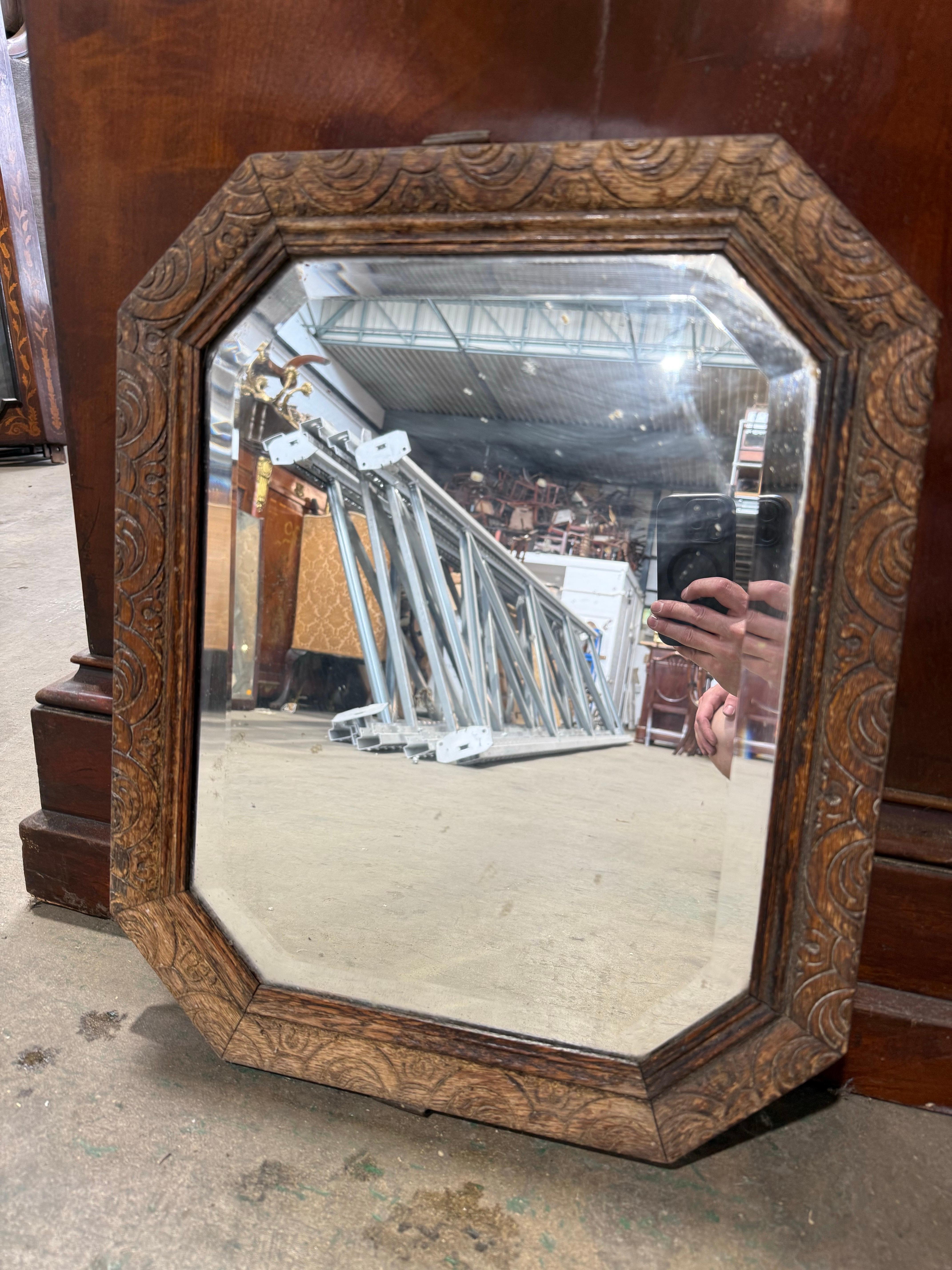 Bellissimo specchio da parete del XIX secolo con cornice ottagonale in Oak intagliata a basso rilievo con motivi fogliacei. La patina calda e le ricche venature del rovere conferiscono un fascino rustico, mentre i bordi smussati del vetro a specchio