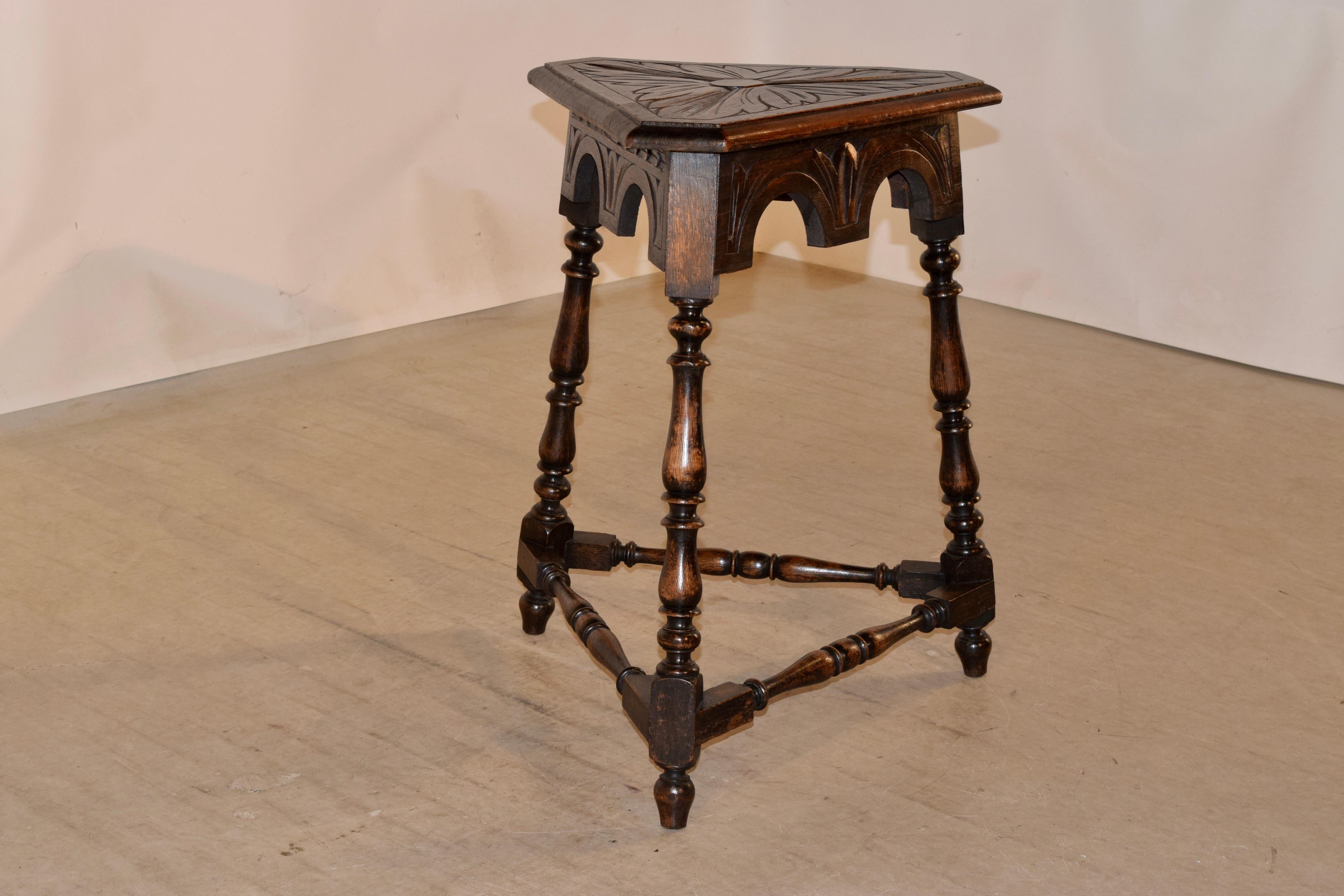 19th century oak side table from England with a triangular shaped top which has a beveled edge and lovely carved top. This rests upon a scalloped and carved decorated apron and splayed hand-turned legs, joined with matching stretchers.