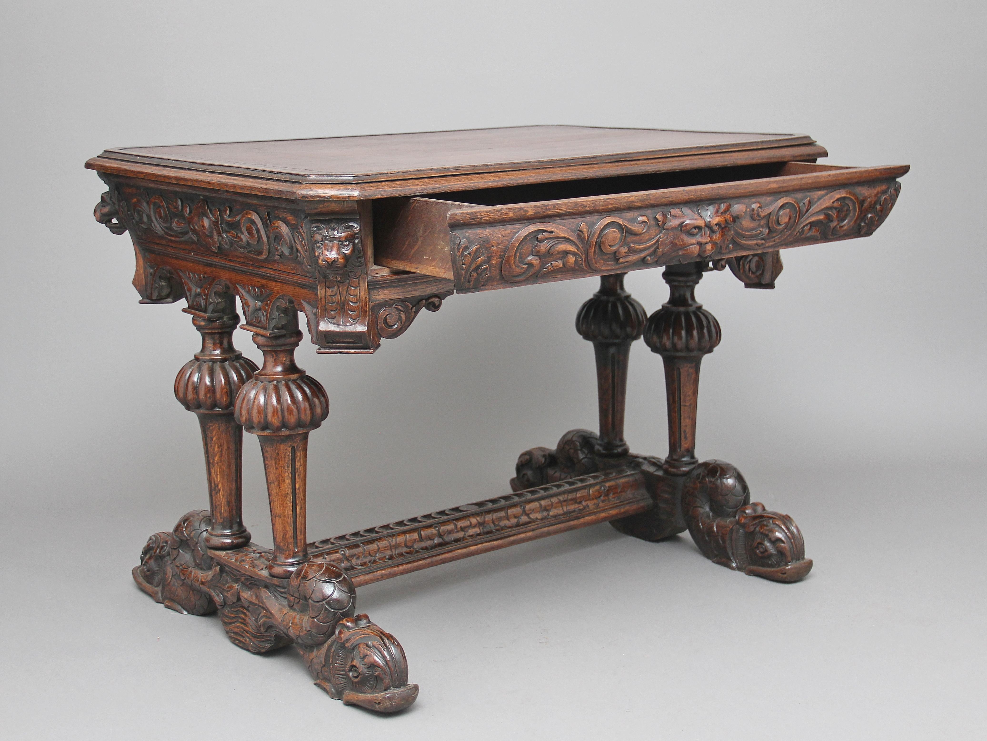 19th century carved oak writing table with one drawer in a heavily carved frieze, with lions heads on the corners and a grotesque mask as a handle, supported on twin columns and carved dolphins united by a stretcher, the moulded and crossbanded top