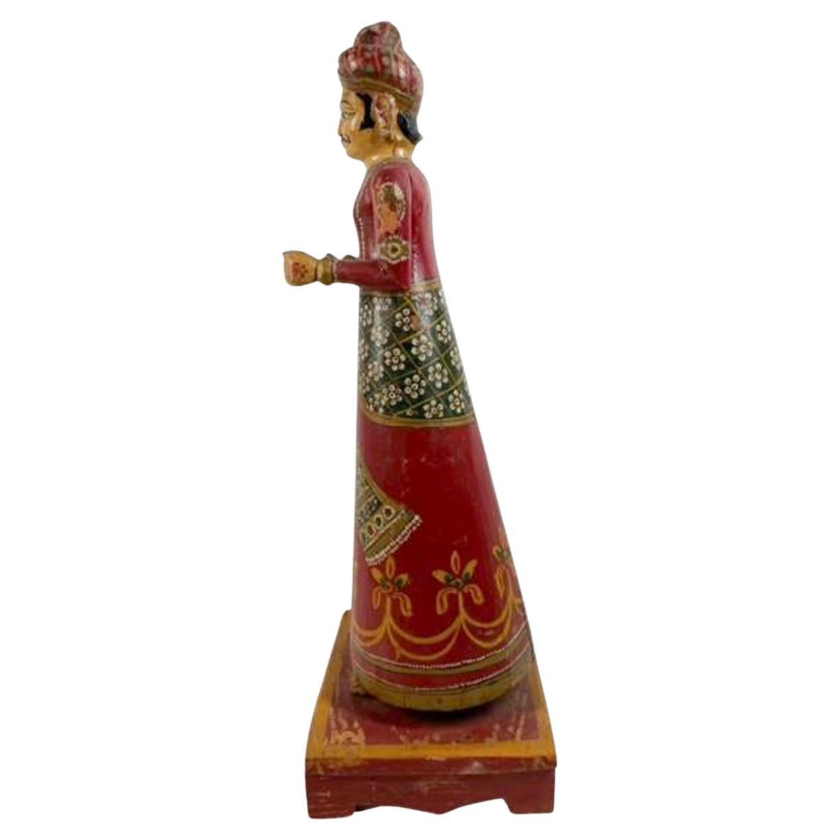 Figure en bois peint et sculpté représentant un gentleman en robe et turban ornés de bijoux, debout sur une estrade et les mains tendues, peut-être dans un geste d'offrande. Peut-être une figure de cérémonie ou de procession. Pertes aux doigts.