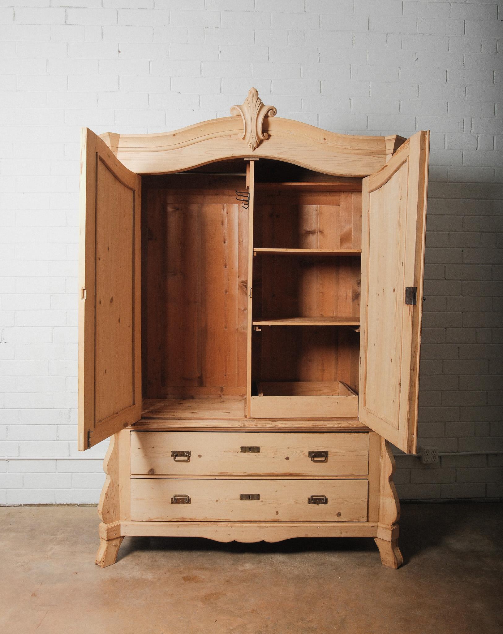 Dieser handgefertigte Schrank ist vollständig aus massivem Kiefernholz gefertigt und verfügt über einen wunderschön geschwungenen Giebel mit zentralem Wappendetail. Die beiden großen vertäfelten Türen mit fließenden Konturen lassen sich öffnen und