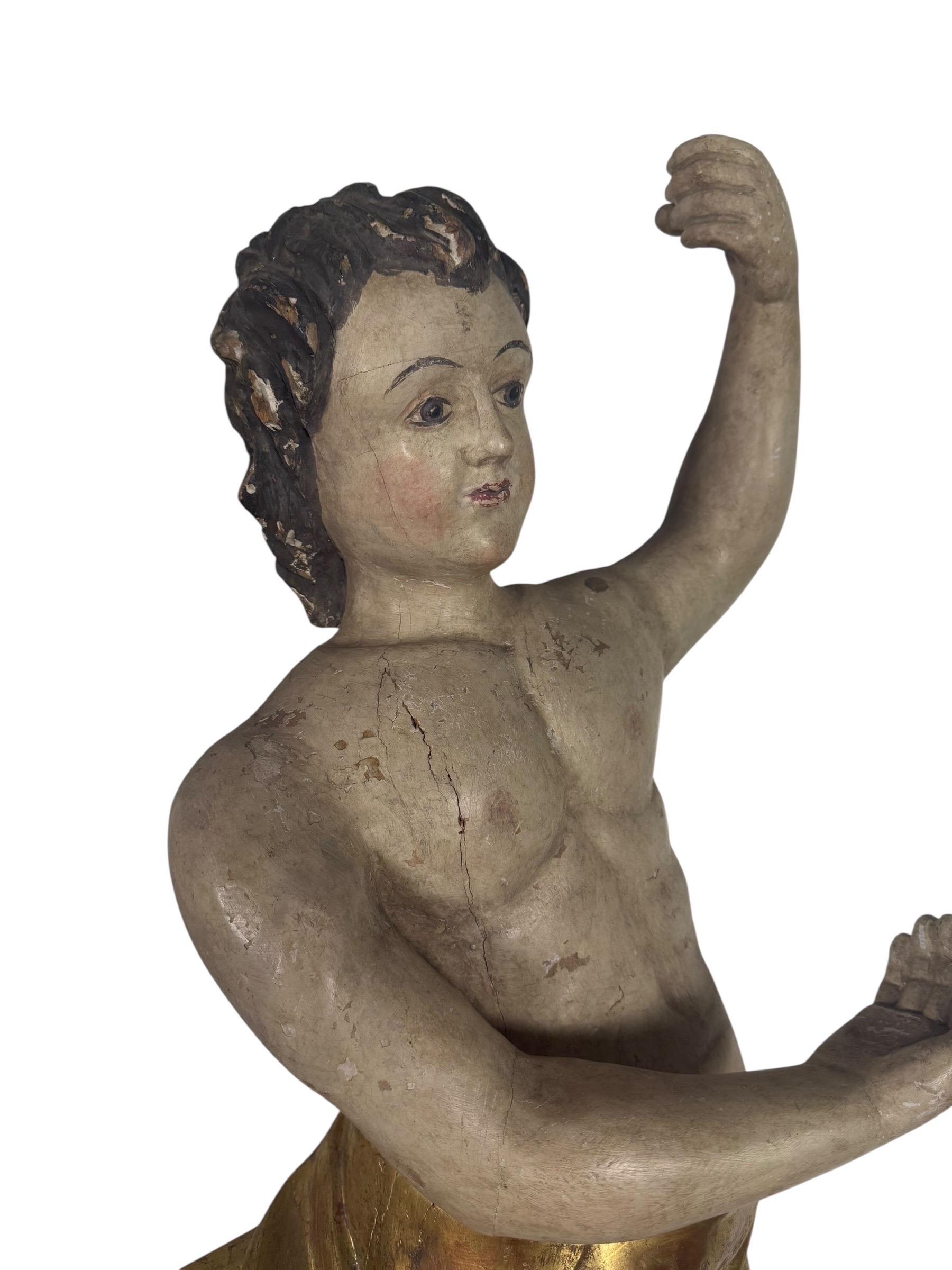 A finely carved polychrome and giltwood figure depicting a lively putti (cherub), shown in dynamic motion with one arm raised and the other curved across the chest. The youthful figure is rendered with delicately modeled features, softly painted