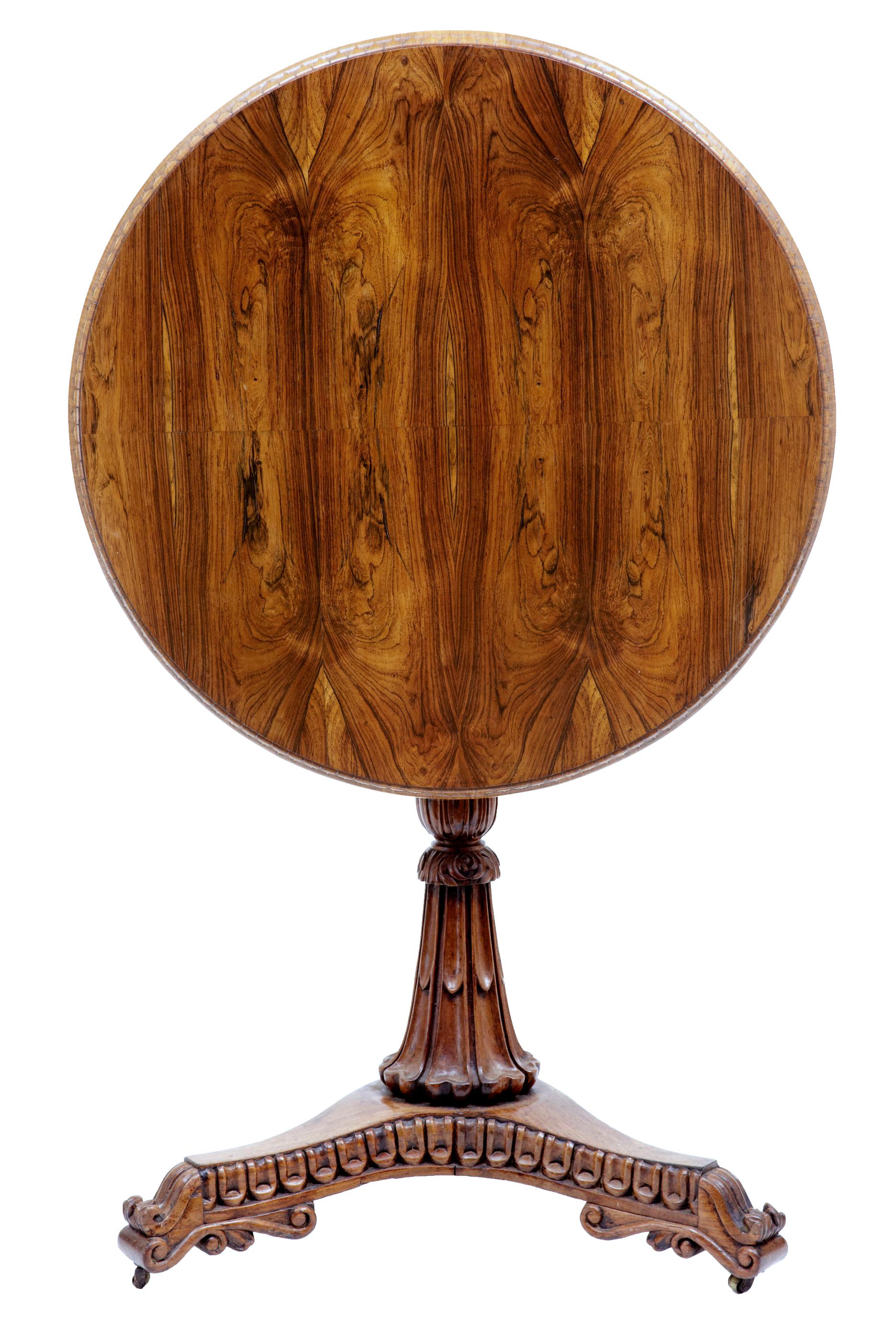 Circular occasional table veneered in striking palisander, decorated with a carved outer edge.

Turned and carved stem standing on a carved tripod base with scrolled feet and brass castors. Tilting top.

Rich golden color.

Minor surface marks