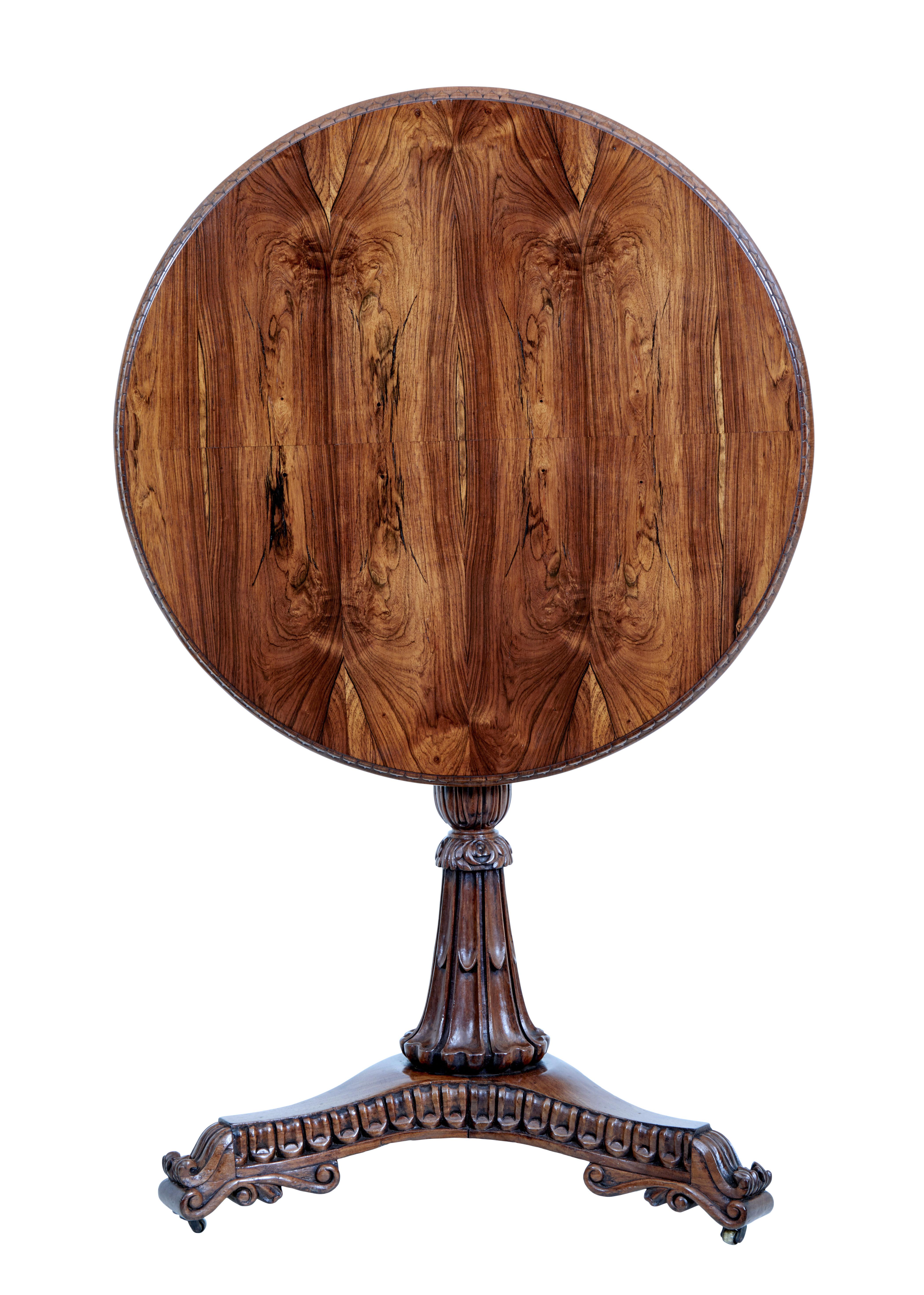 Circular occasional table veneered in striking palisander, decorated with a carved outer edge.

Turned and carved stem standing on a carved tripod base with scrolled feet and brass castors. Tilting top.

Rich golden colour.

Minor surface