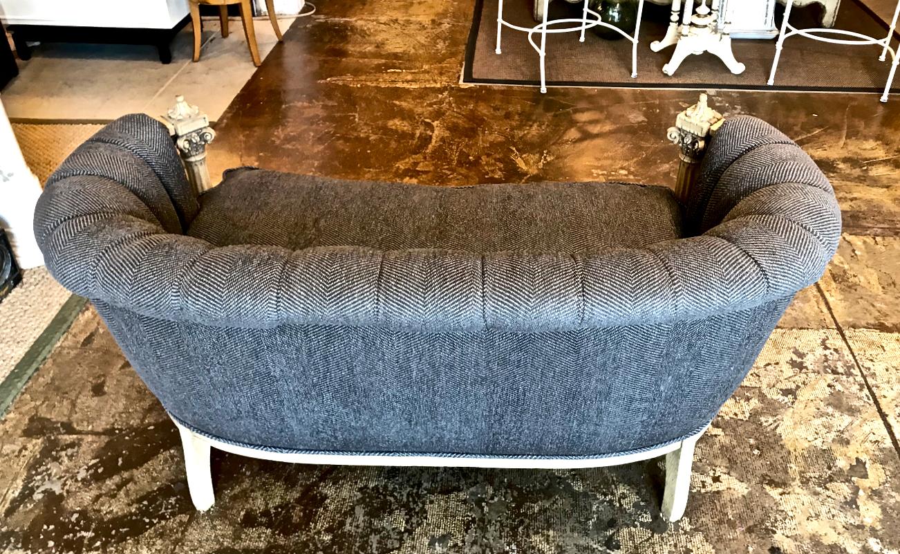 This is a unique, if not slightly funky, highly carved bleached mahogany small sofa or settee that is newly upholstered in a Kravet herringbone tweed. The very masculine herringbone adds the perfect contrast to the Corinthian column meets