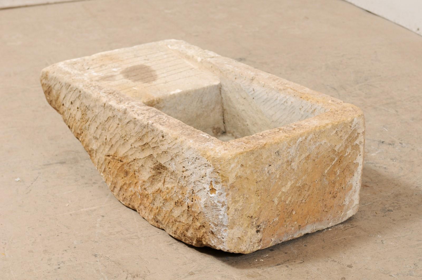 A European large stone sink with side drainboard from the 19th century. This antique sink from Europe has an overall rectangular shape and has been hand carved from a single piece of stone. One side of the sink has a drainboard, which tilts into the