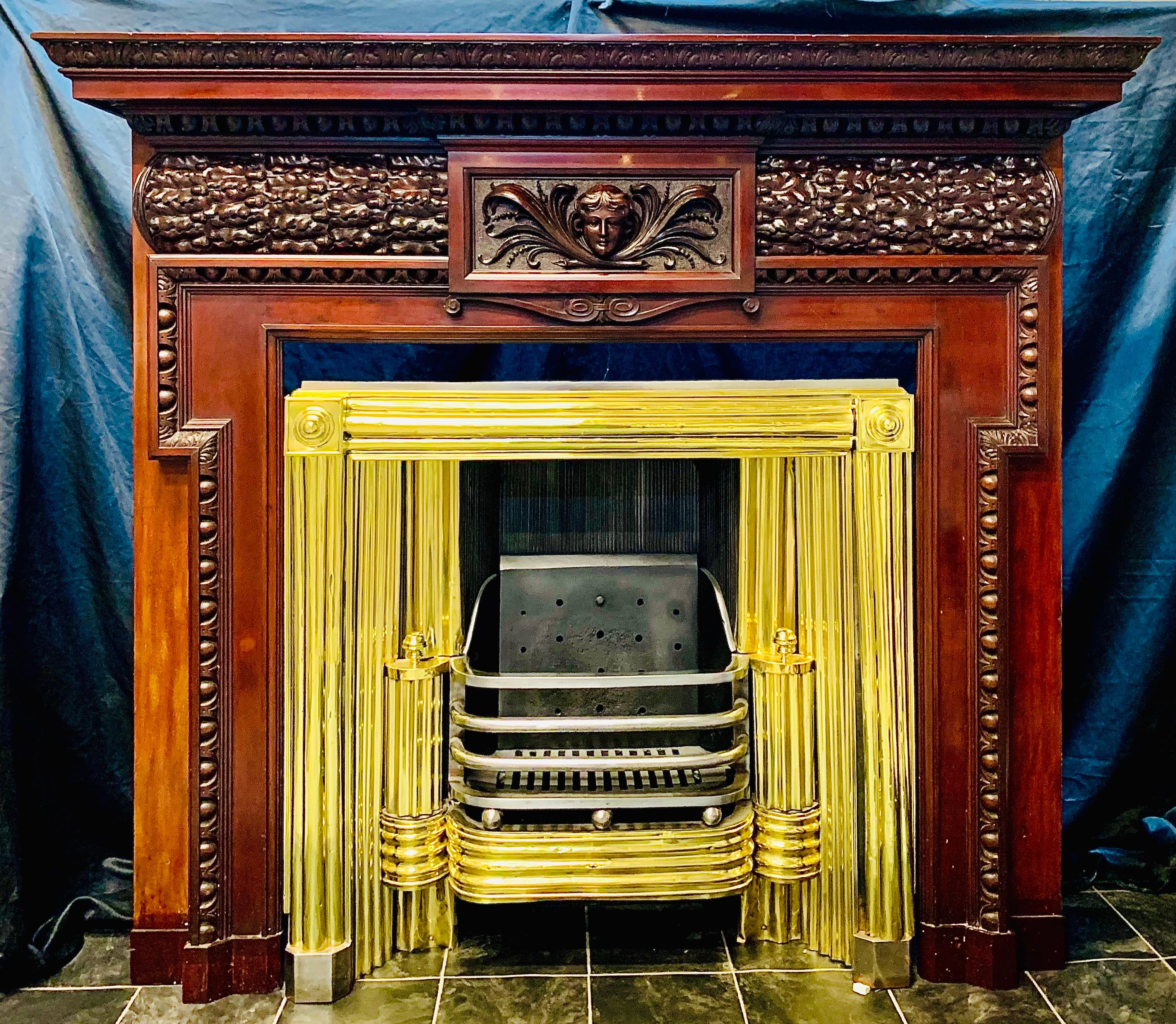 A large and inherently grand late 19th century finely carved walnut fireplace surround in the Georgian manner. A substantial moulded and carved top shelf over a central profusely carved female mask with an under cartouche -flanked either side by