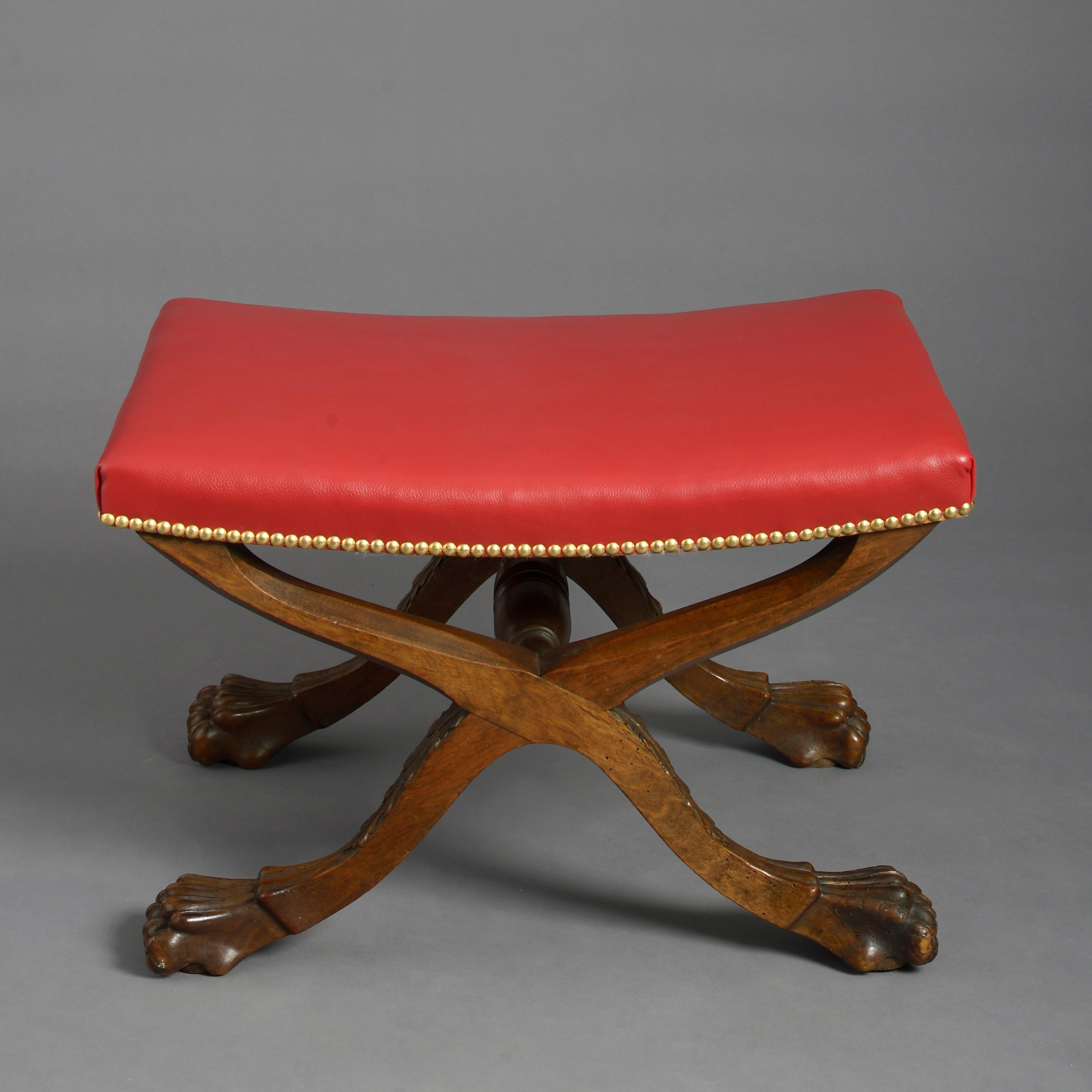 A mid-19th century early Victorian Period carved walnut X-frame stool, the supports with carved stylised acanthus leaves and paw feet with turned central stretcher, the shaped leather upholstered seat with brass nailing.