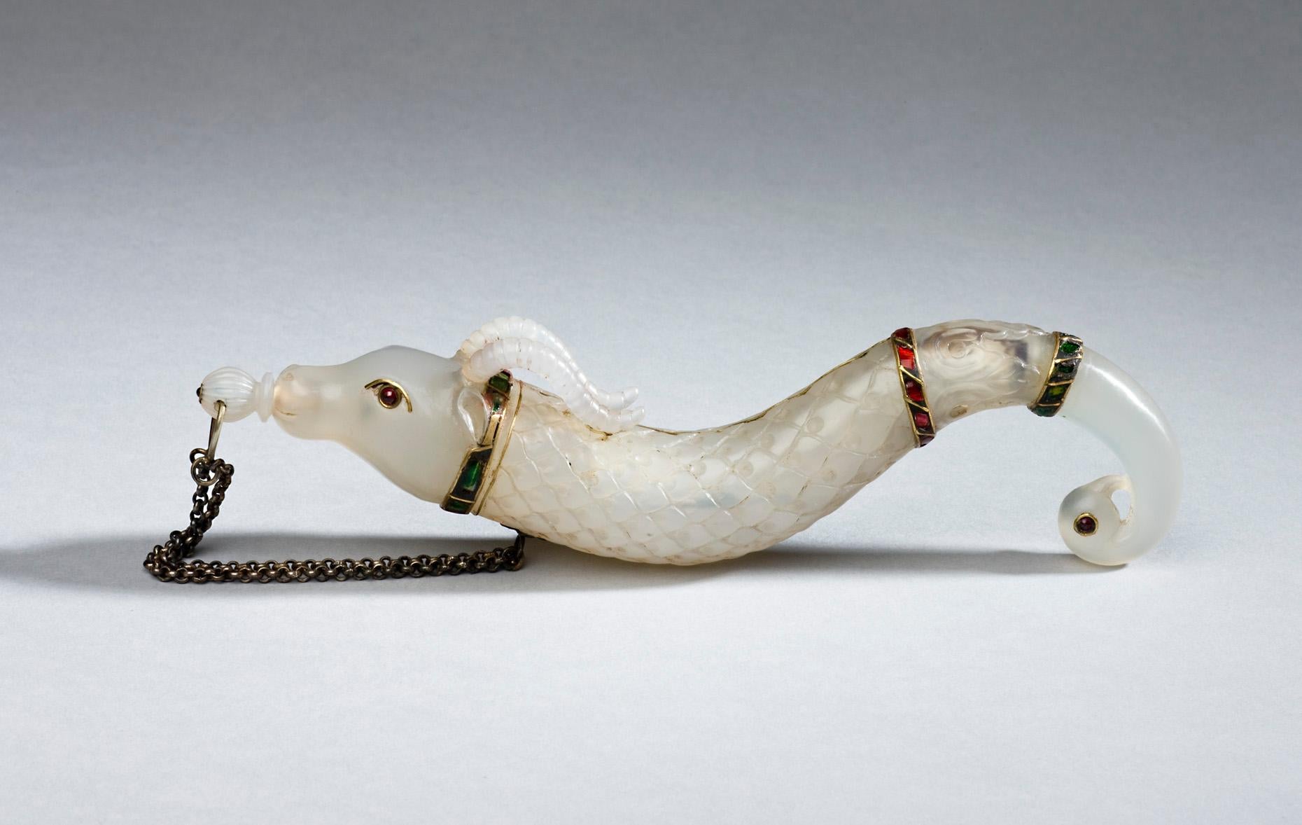 Exquisite carved white jade powder flask as a caribou-like form with red rubies eyes, body carved in shell design and decorated with red rubies and green emeralds bands, ends in the form of a parrot with red rubies eyes.