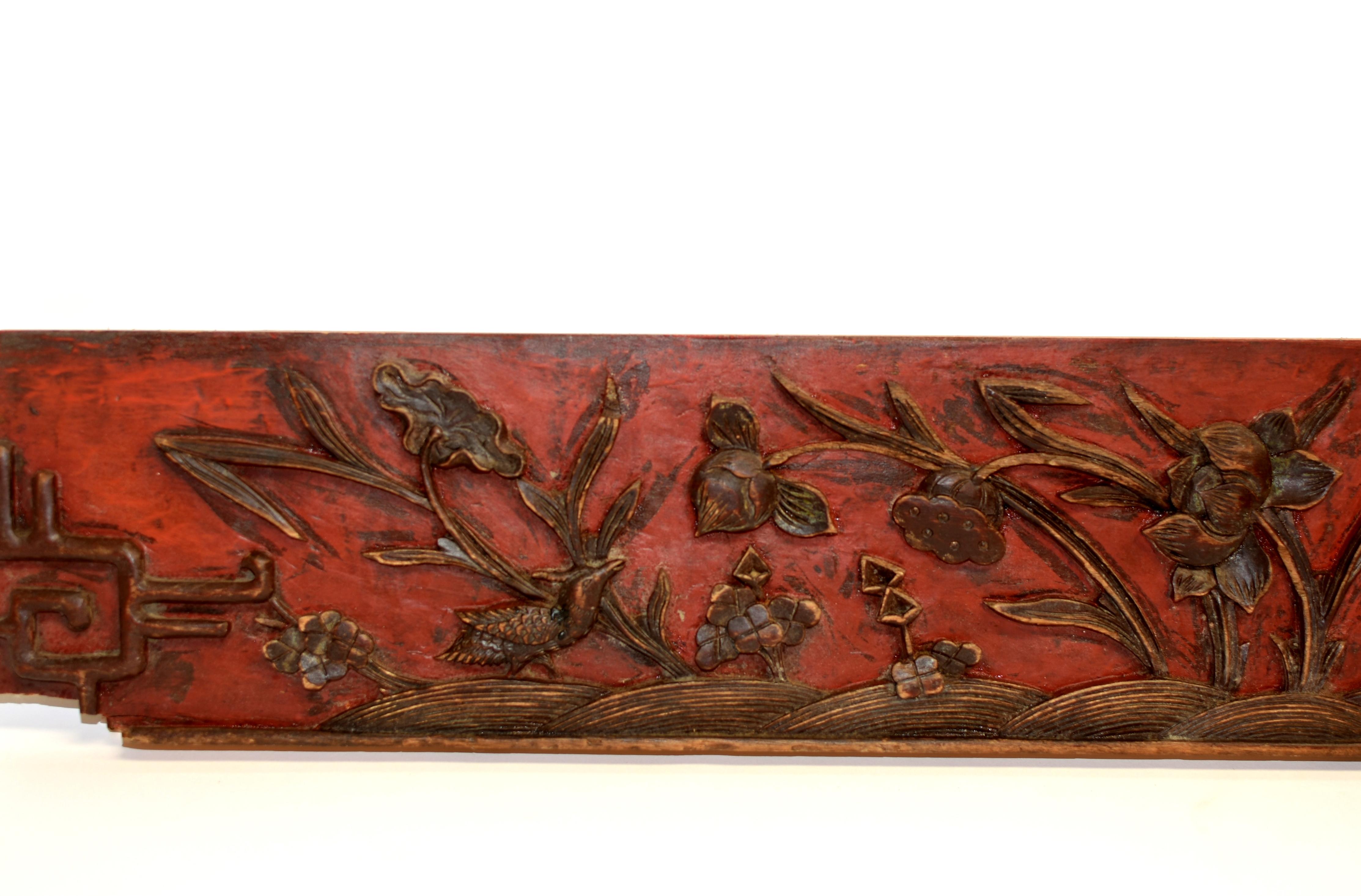 A solid wood panel with deep relief carvings of lotus in various stages of blooming. A pair of birds with one in motion of landing and the other on the ground echoing each other. On red lacquered background is a field of water irises with their