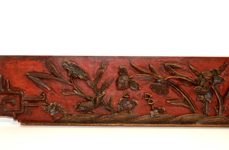 A solid wood panel with deep relief carvings of lotus in various stages of blooming. A pair of birds with one in motion of landing and the other on the ground echoing each other. On red lacquered background is a field of water irises with their