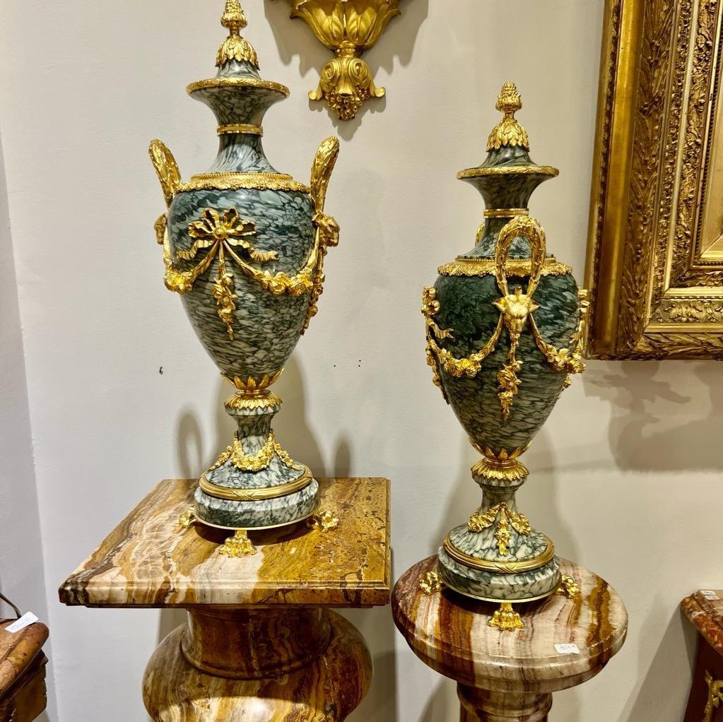 We present you this wonderful pair of cassolettes, urns in English, in gray-green ash-colored marble veined with white. They feature a highly decorative gilded bronze mount adorned with ram's heads, garlands, claw feet, laurel leaf handles, and