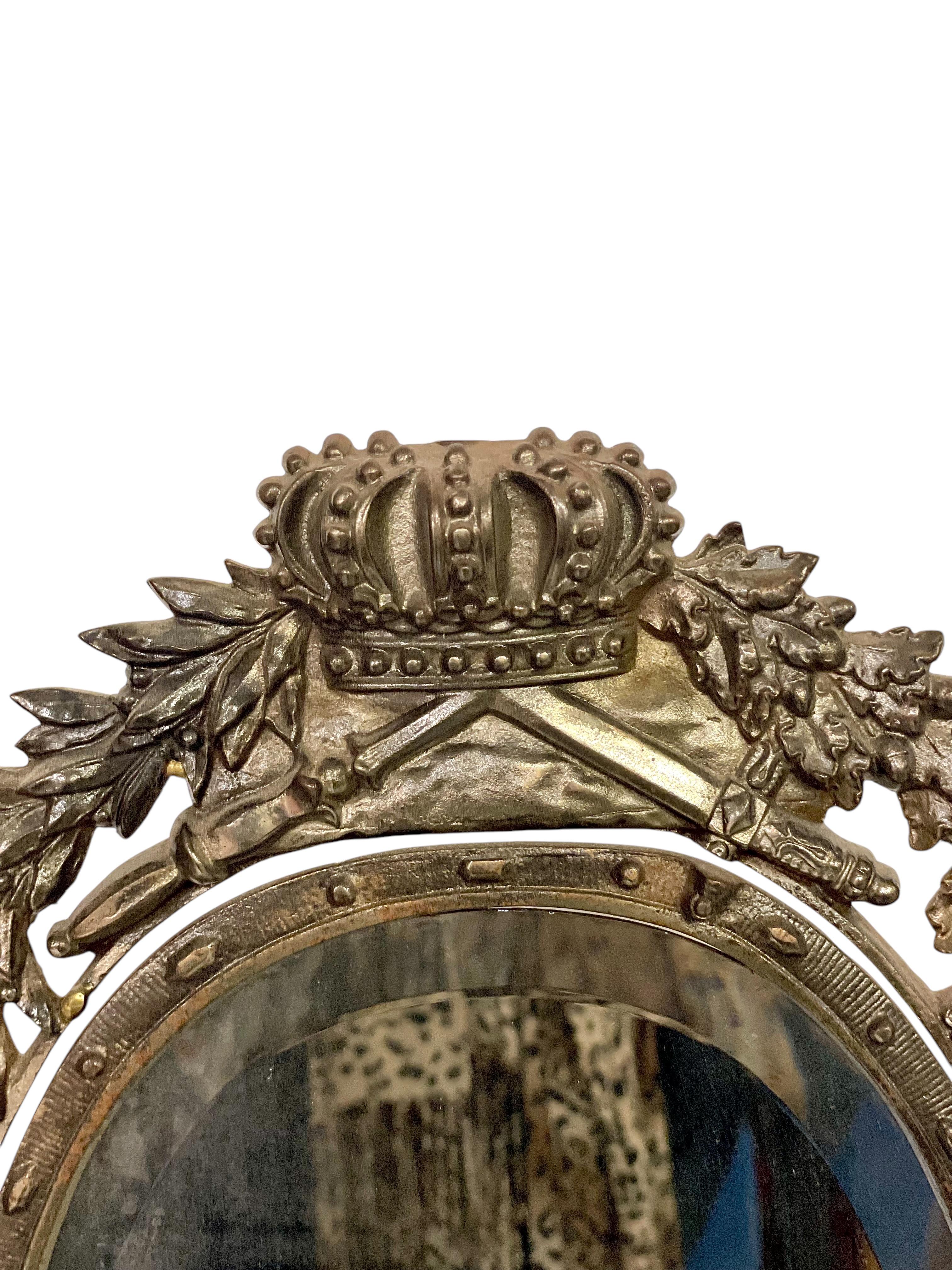 Ce remarquable miroir de table français du XIXe siècle est coulé dans un métal lourd et richement orné de motifs héraldiques détaillés. Le cadre est surmonté d'une couronne de style royal reposant sur des bannières croisées et des feuilles de