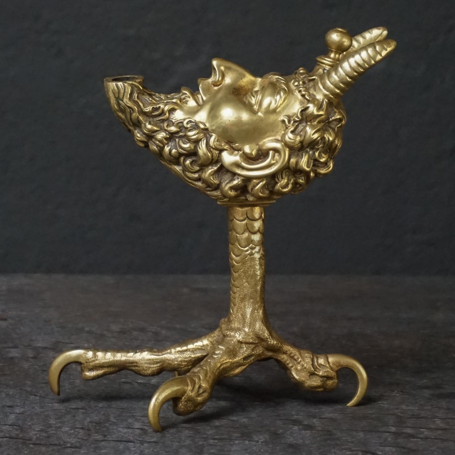 Very unusual 19th century brass table or counter top cigar lighter. 
Finely cast brass satyr or devil head on a rooster leg or talon with an oil reservoir, once filled it can be used to light your cigar from a burning wick from his mouth. 
Rare