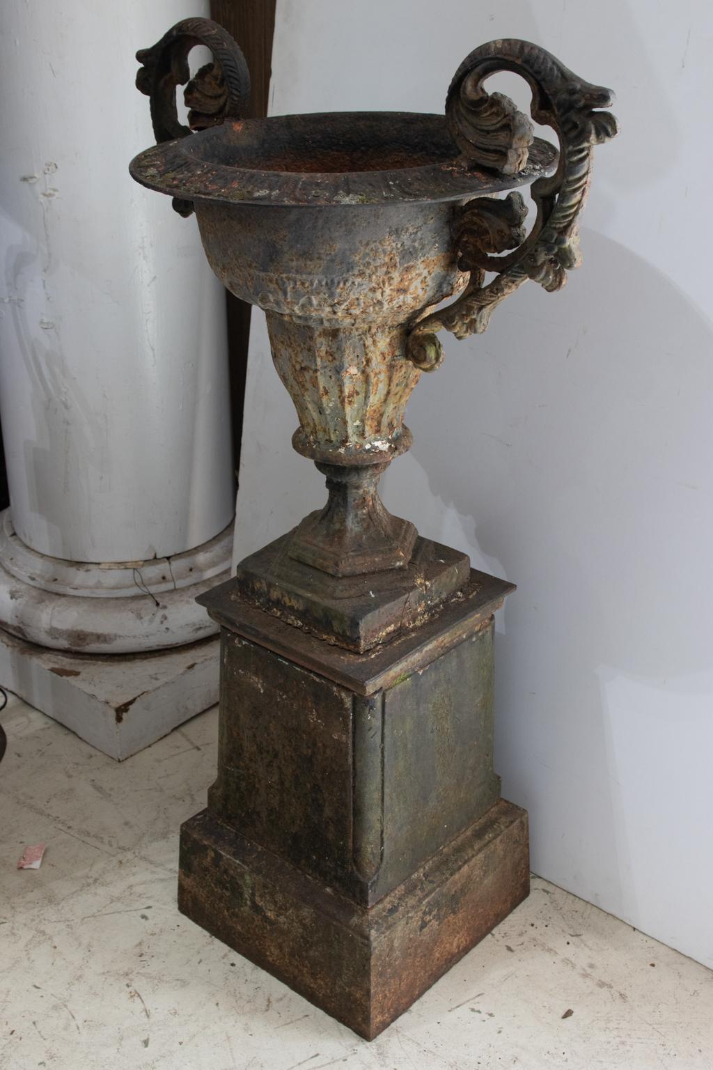 Circa 19th century cast iron urn on plinth base with double handles. Please note of wear consistent with age and exposure to the elements such as patina and oxidation throughout.