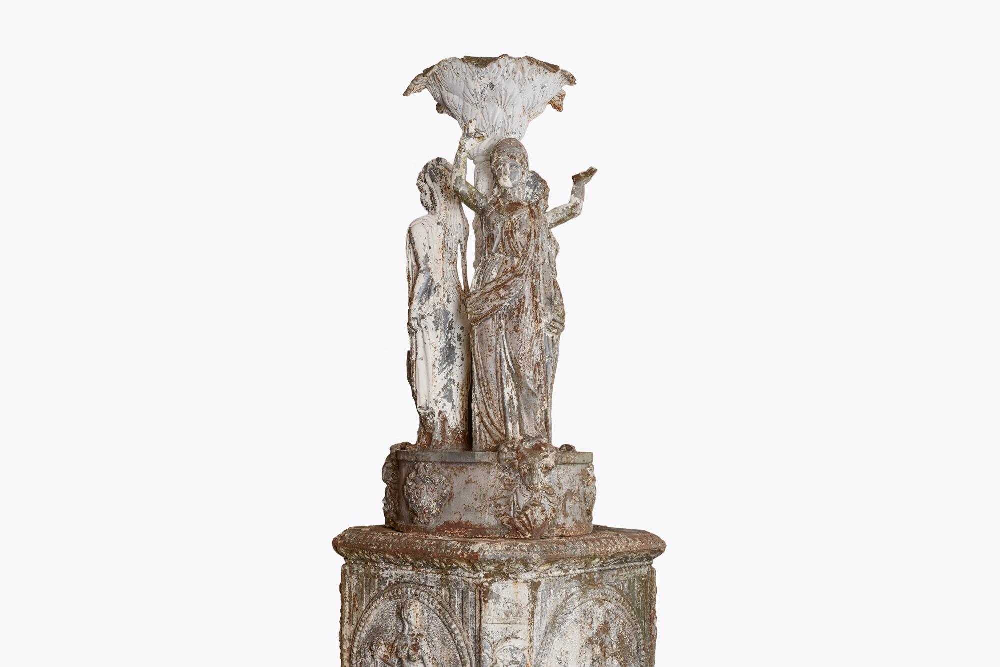 19th Century cast iron garden monument depicting the three graces Diana, Venus and Athena surrounding an ornately decorated font with foliate motif, held on round base with shells and ram heads, above a square platform with vignettes of female