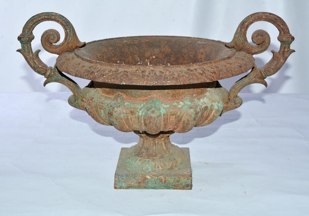 The round Victorian cast iron jardinière has a pair of decoratively scrolled handles, a flared rim, fluted basin with a hole in the bottom for drainage. The basin sits on a square base. Residue of original green paint.

Height to handle: 11.50