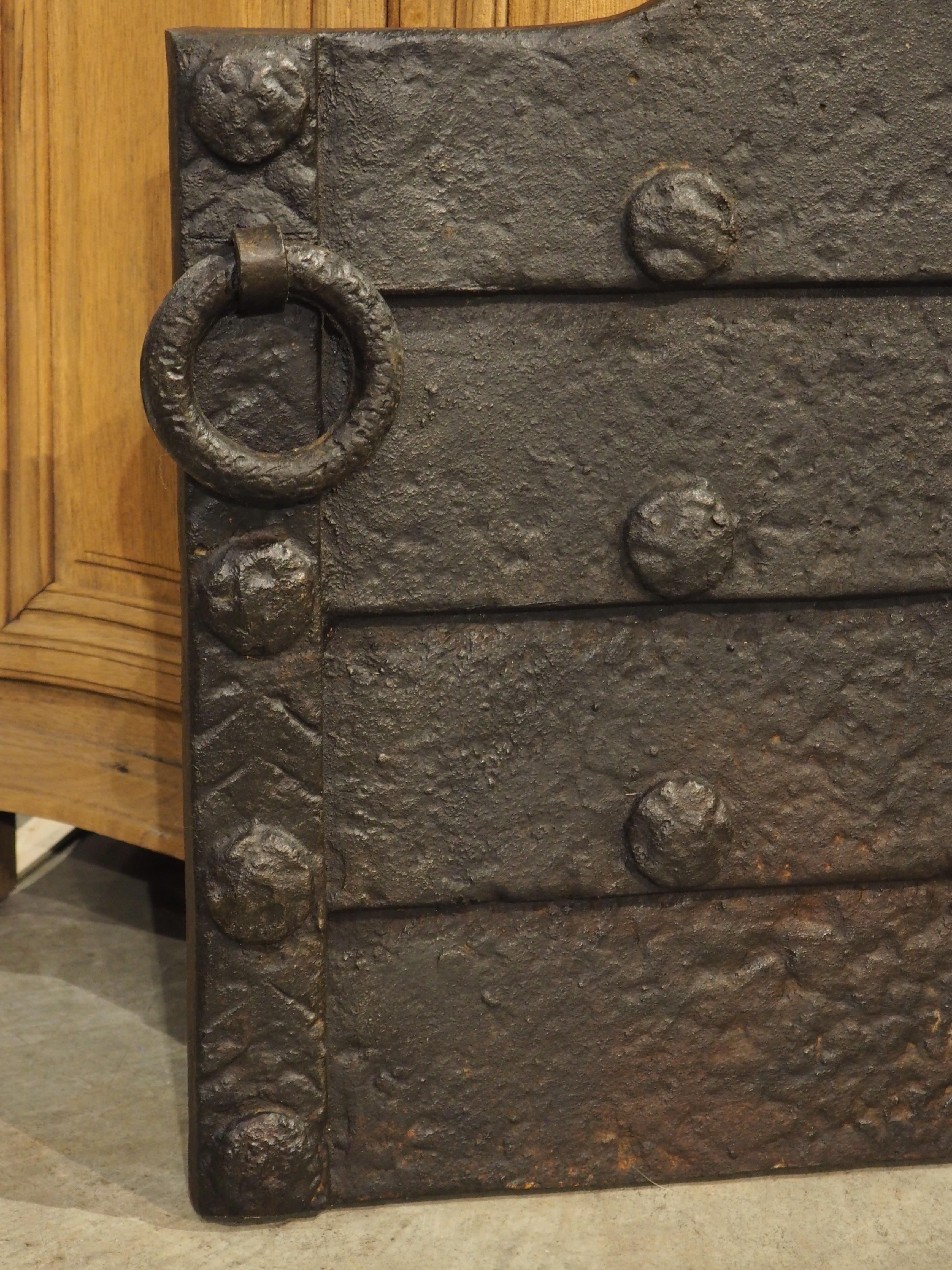 Cast in the 1800s in the Medieval style, this robust French iron fireback features thick horizontal, lapped plates that comprise the fireplace accessory. The fireback is roughly rectangular, with an arched top that softens the linear form. A pair of