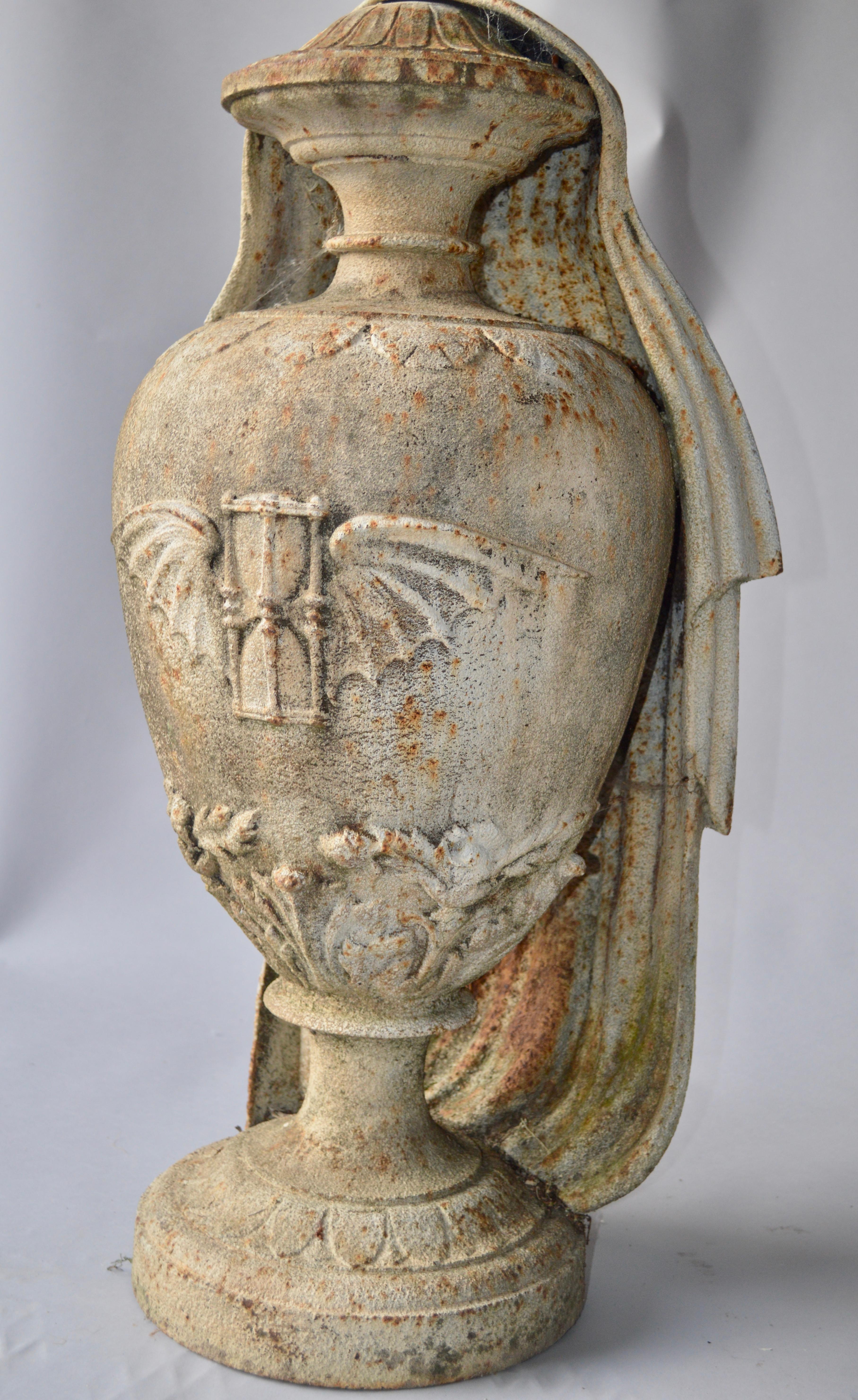 19th century cast iron urn with motive of bat and hourglass and backside draped in cloth.