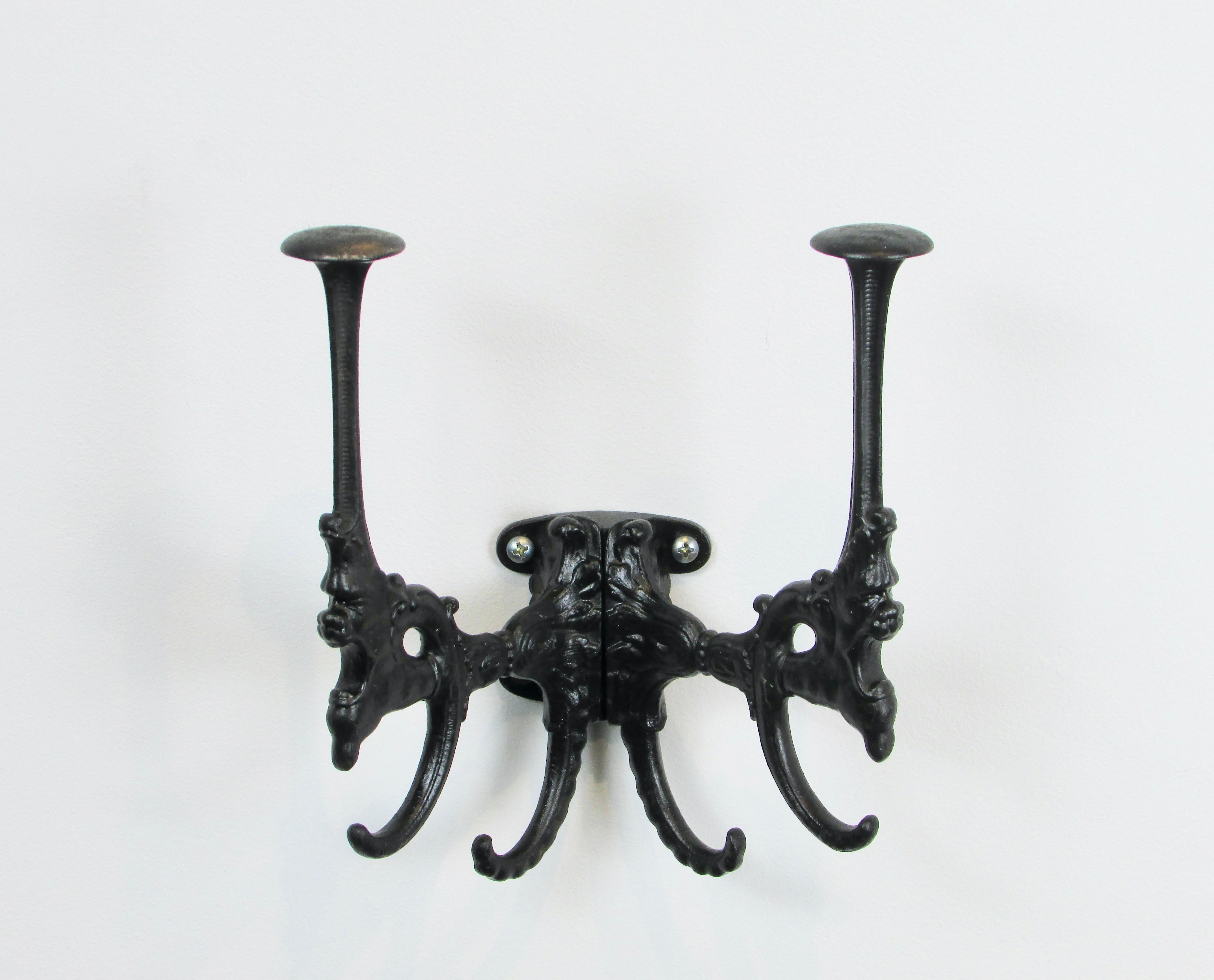 Small wall mounted hat rack with lots of character . Cast iron embellished with gargoyle heads finished in matte black . One of the lower ears for mounting screw has been lost to time . 