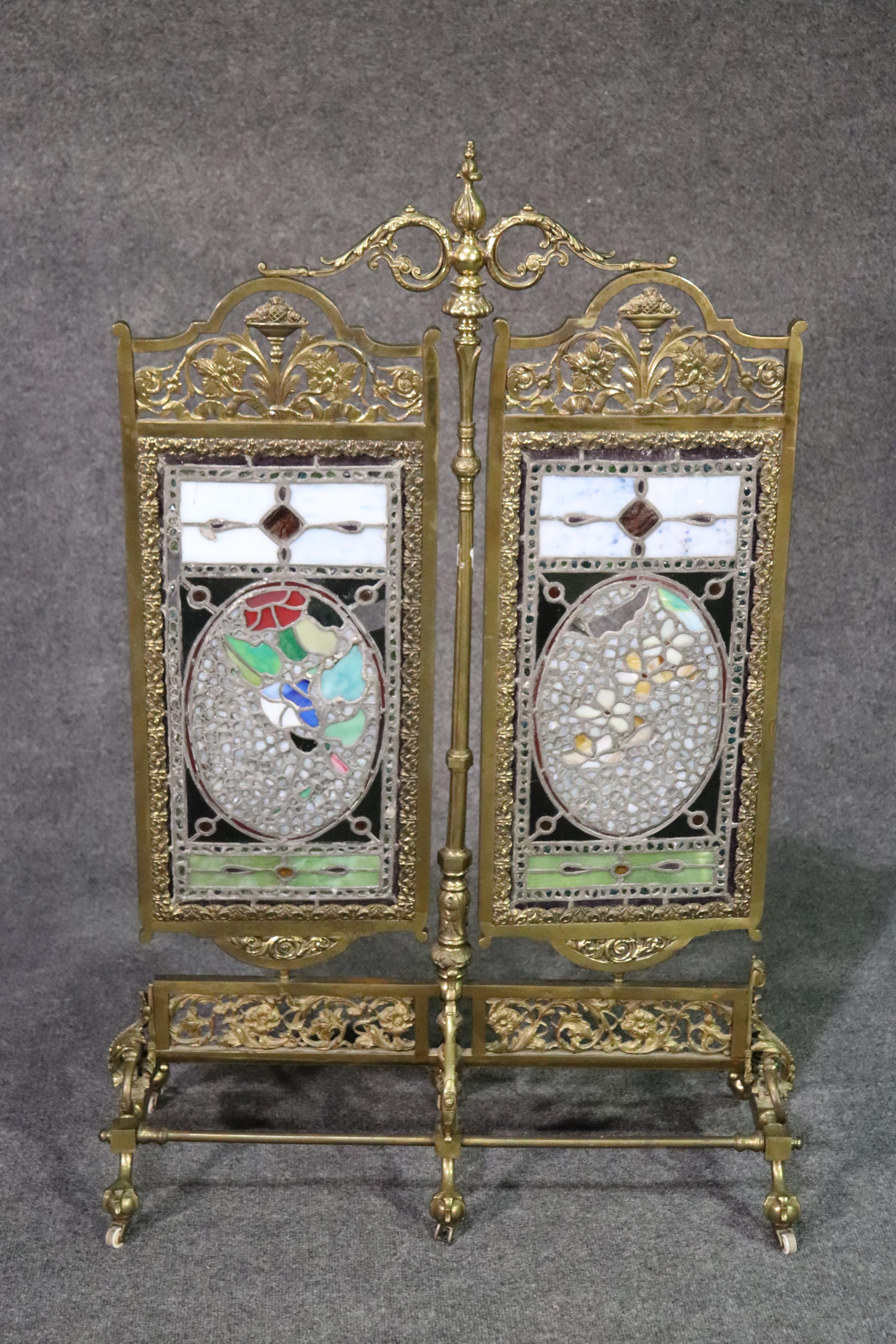 This is a very rare and unique American Victorian stained glass firescreen. The articulating moving panels depicting flowers and jeweled pieces of stained glass. Two small stained glass pieces are missing. The frame is done in the finest cast brass