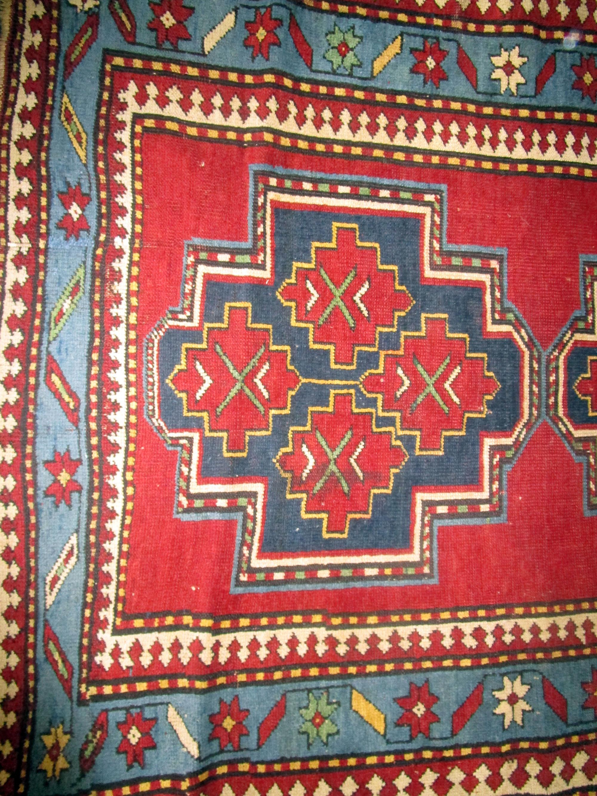 This handsome Kazak rug features a double large, bold, dominating geometric pattern with a smaller patterned within. The detailed borders and backdrop give it an edge that differentiates it from other rugs on the market. The colors used are vibrant