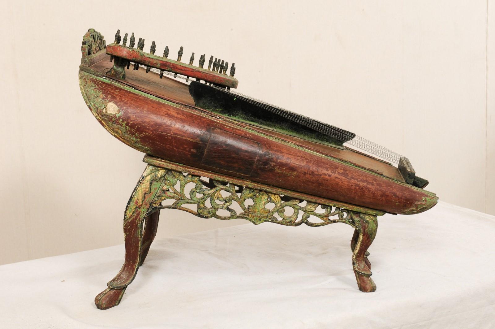 A traditional string musical instrument from Java, late 19th century. This antique celempung from Java, Indonesia has a beautifully decorated wood body, with pierced and carved skirt undercarriage and raised upon legs that terminate into hoof feet.