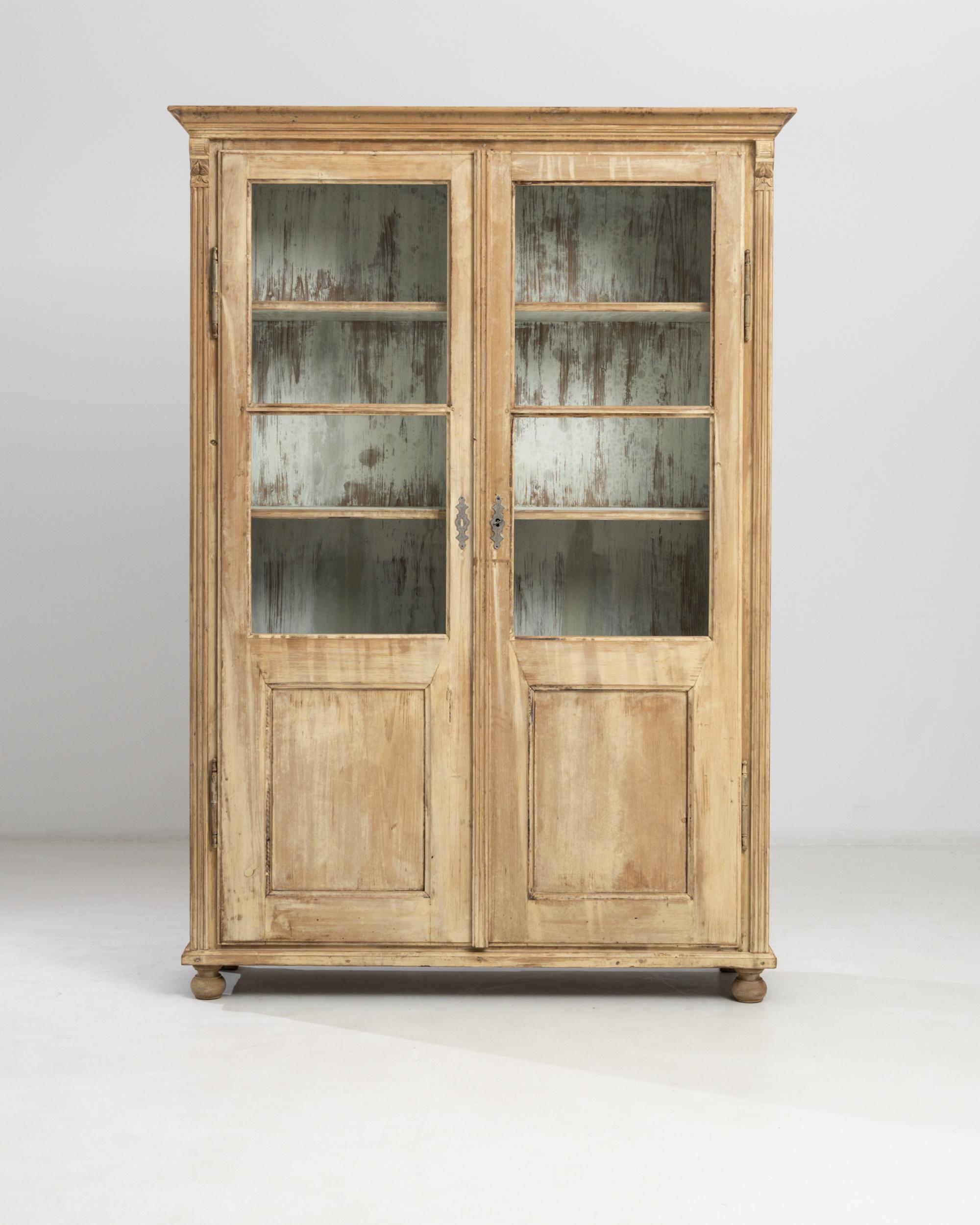 A pair of 19th century wooden vitrines from Central Europe. These tall antique chests feature glass fronts with double-doors and cornice tops, resting on wide bun feet. The four shelf interiors are painted in a pearly white with a charming brushed