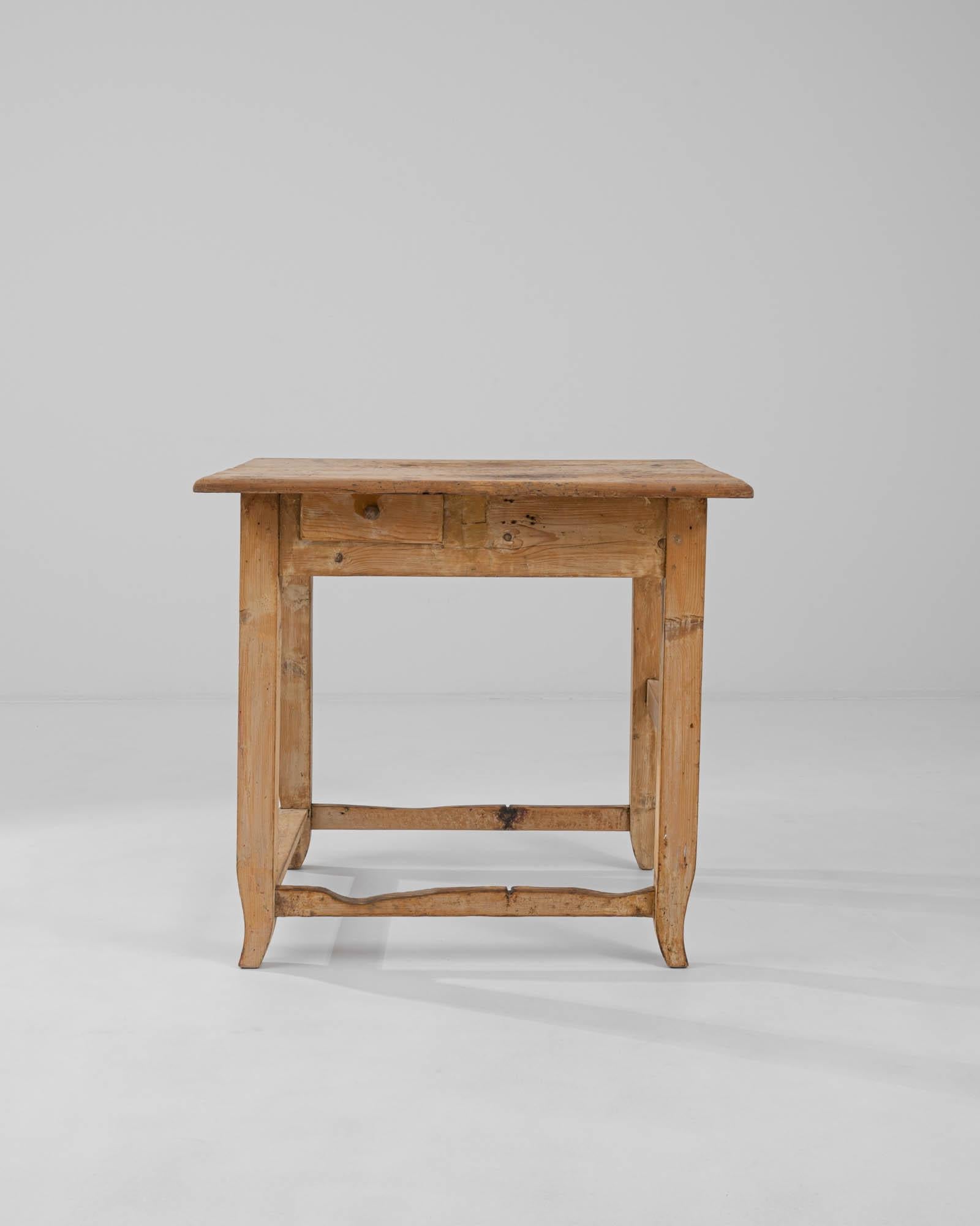 A wooden work table created in 19th century Central Europe. A puzzling piece, this table exerts a charming asymmetry, shining with refreshing and effortless individuality. With one stretcher raised higher than the other three, a playfully offset