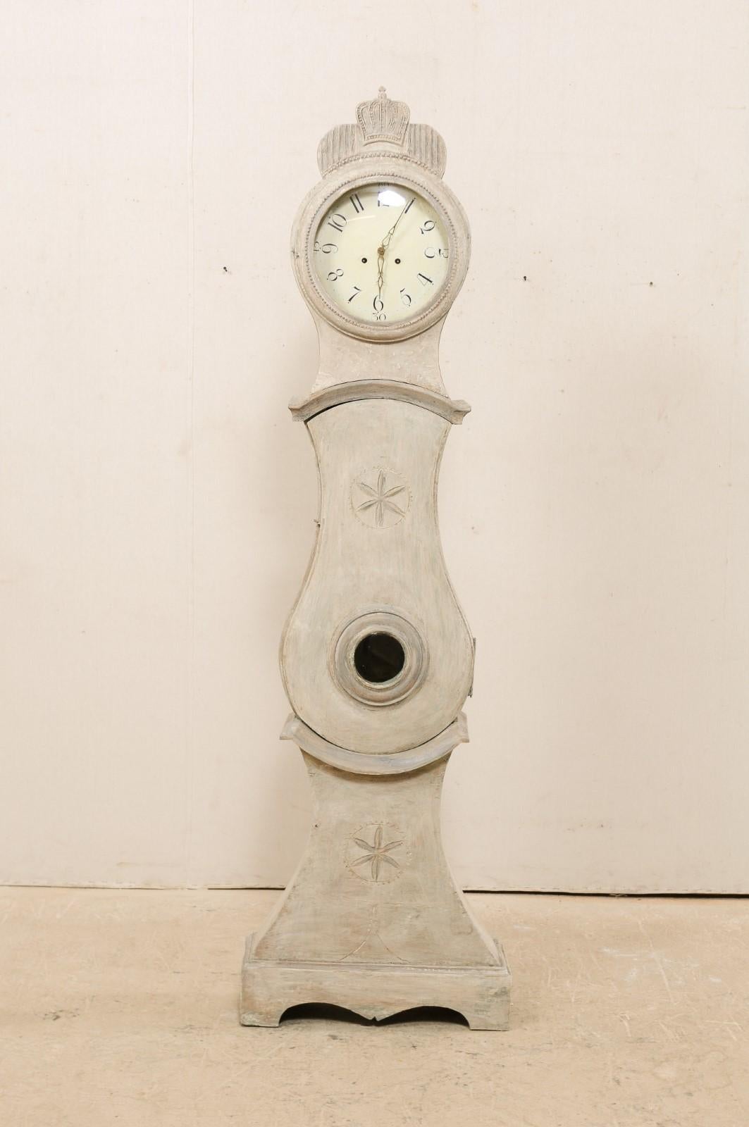 A central Swedish long-case floor clock from the 19th century. This antique floor clock from central Sweden, with its distinct curvy rain-drop shaped belly, is topped with a hand carved crown resting prominently at its crest, and two delicately