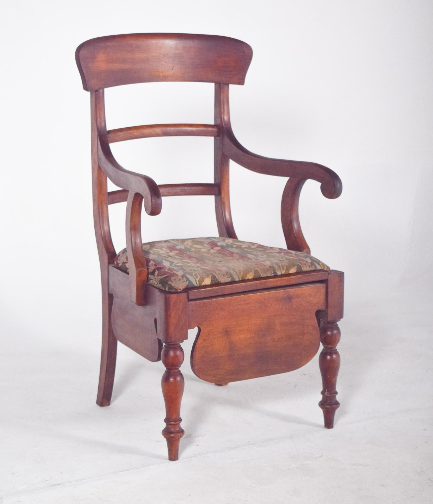 Silla con tapicería a rayas. Con un respaldo de tres travesaños curvos y brazos suavemente arqueados, el asiento tapizado en tela floral revela el uso pensando en la comodidad, y debajo se encuentra el compartimento donde originalmente estaba la