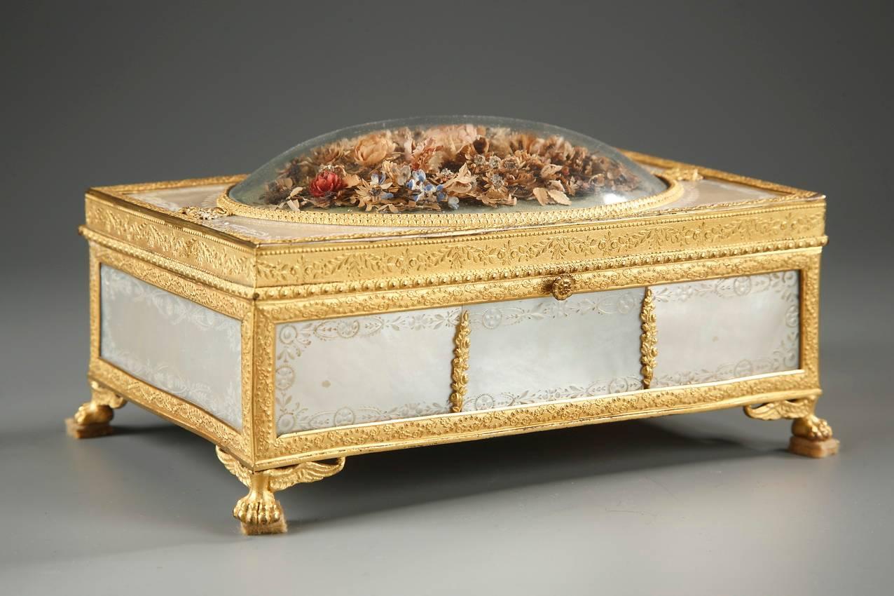 Delicate rectangular mother of pearl box engraved with garlands of leaves. The box is mounted in gilt bronze and intricately sculpted with interlacing, garlands and baskets of flowers. It rests on four winged lion paws. The lid is decorated with a