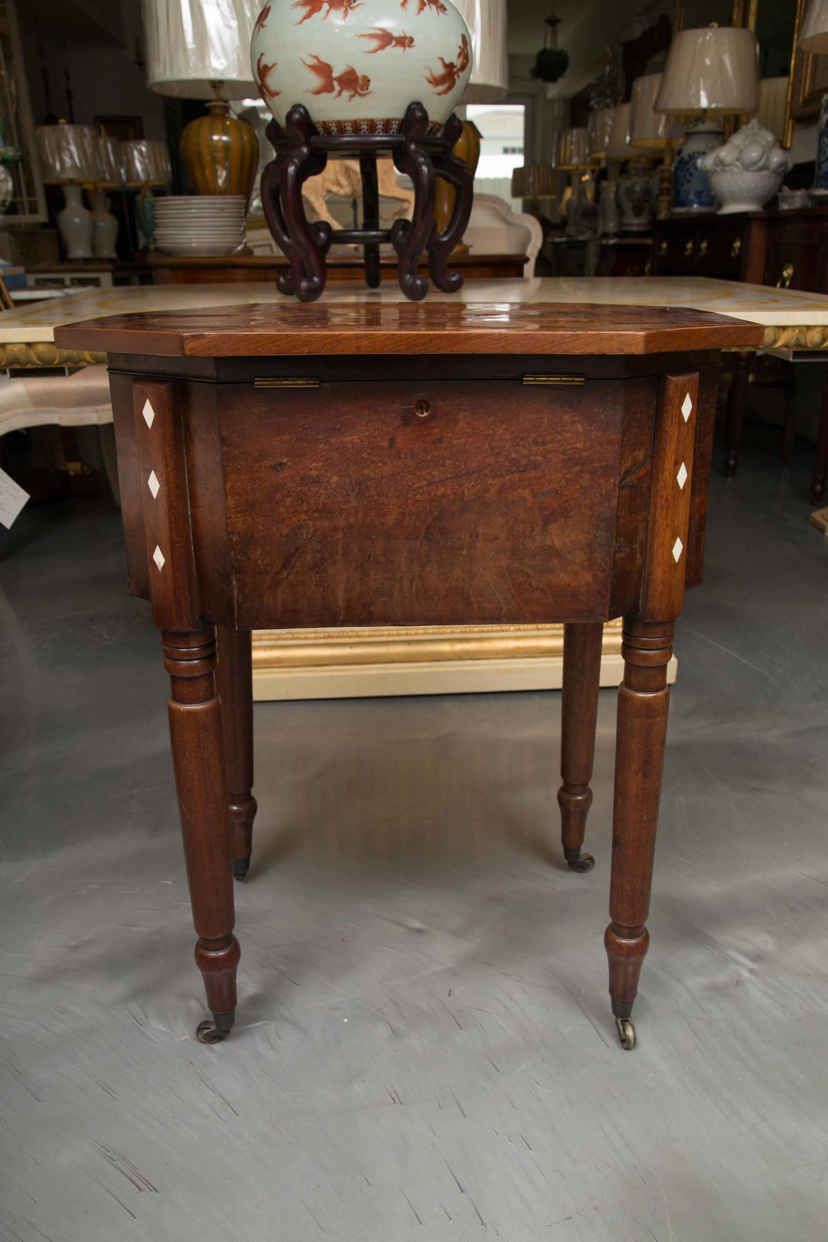 This is a very collectible period Charles X mahogany sewing table. There is a lift top with canted corners and pie-shaped veneers centered by an inlaid checker board above a bank of three drawers with decorative accents. The table is supported by