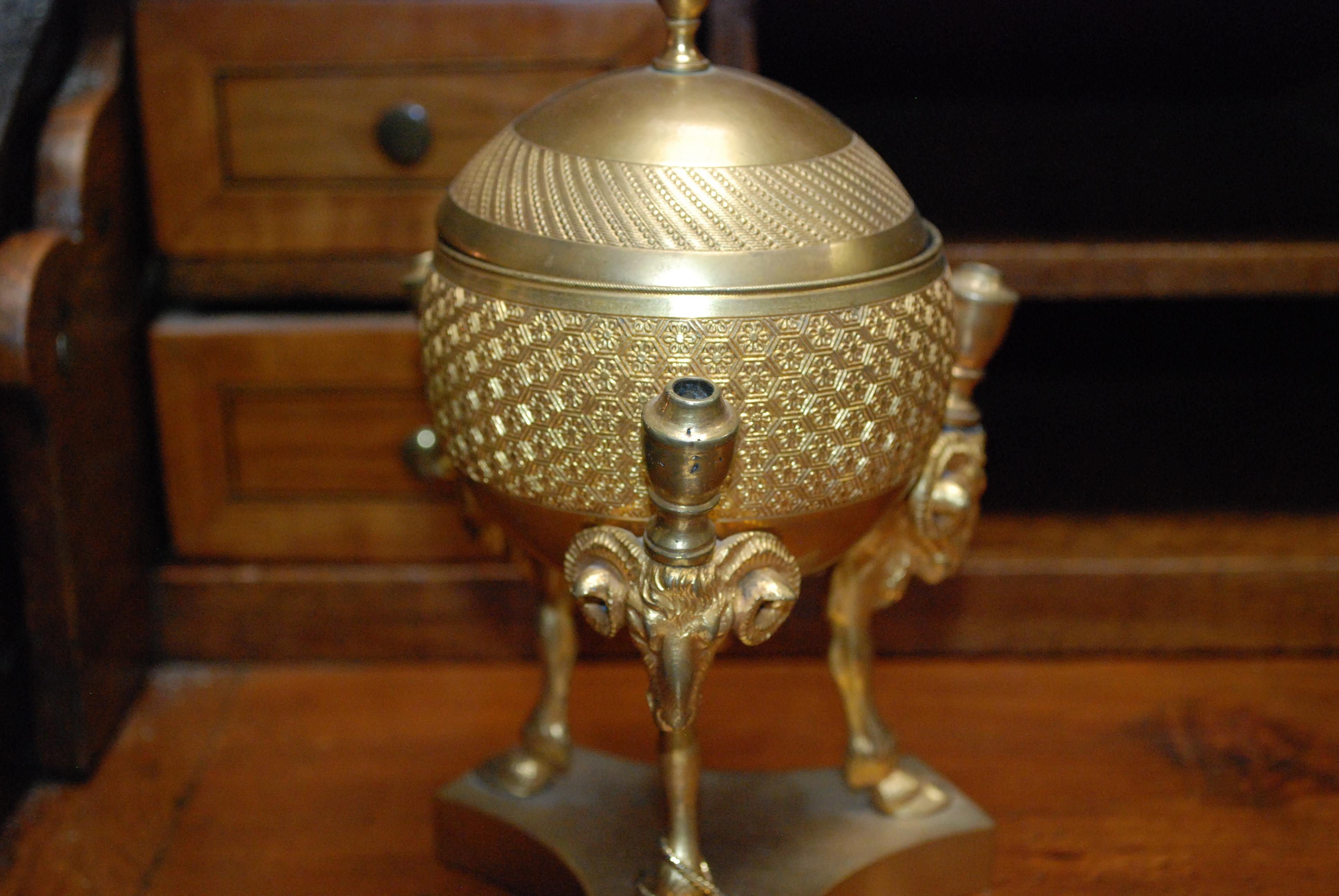 A Charles X ormolu ink stand in the shape of a globe surrounded by three rams head pen supports with animal legs and hoofs on a tripartite base. The top is removable revealing a silvered compartment with containers for sand and ink. Circa 1800.