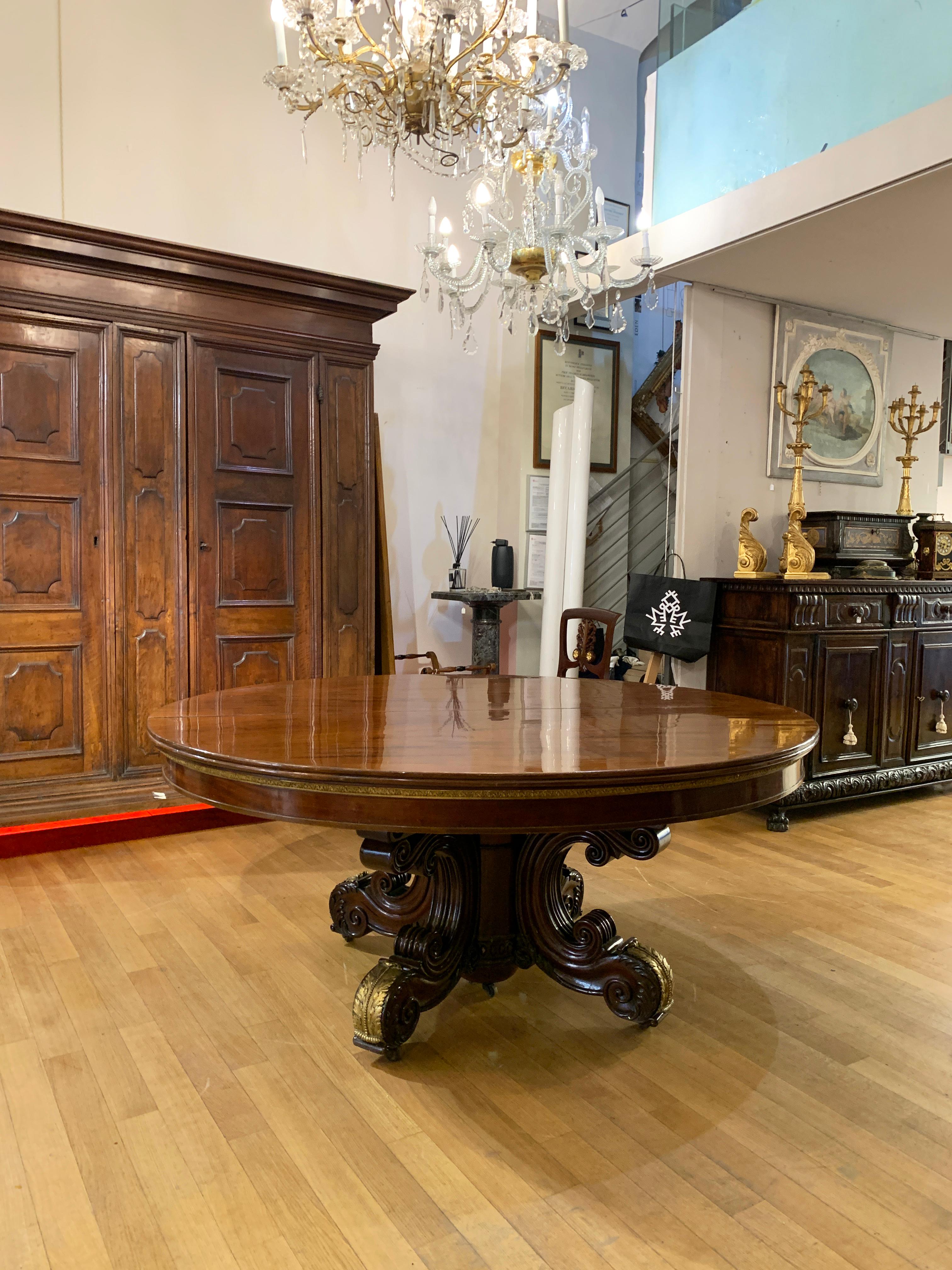 Stunning oval table in solid mahogany with considerable dimensions. The top can be extended using three extensions, with the possibility of extending it up to 3 meters. Below the top runs a band of gilded bronze, with phytomorphic motifs, which